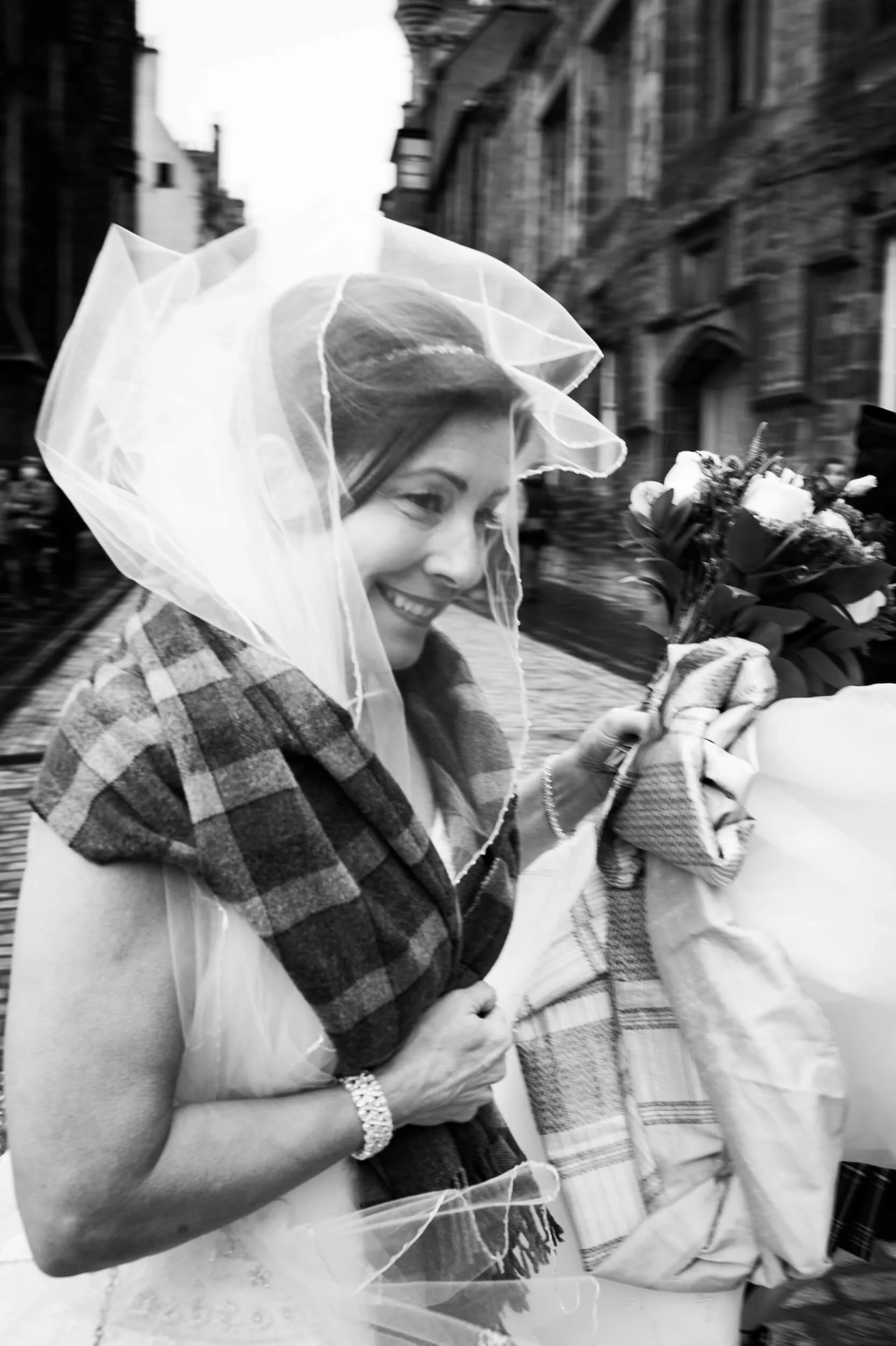 Bride laughing with veil blowing in the wind on the Royal Mile Edinburgh — black and white documentary wedding photography Scotland