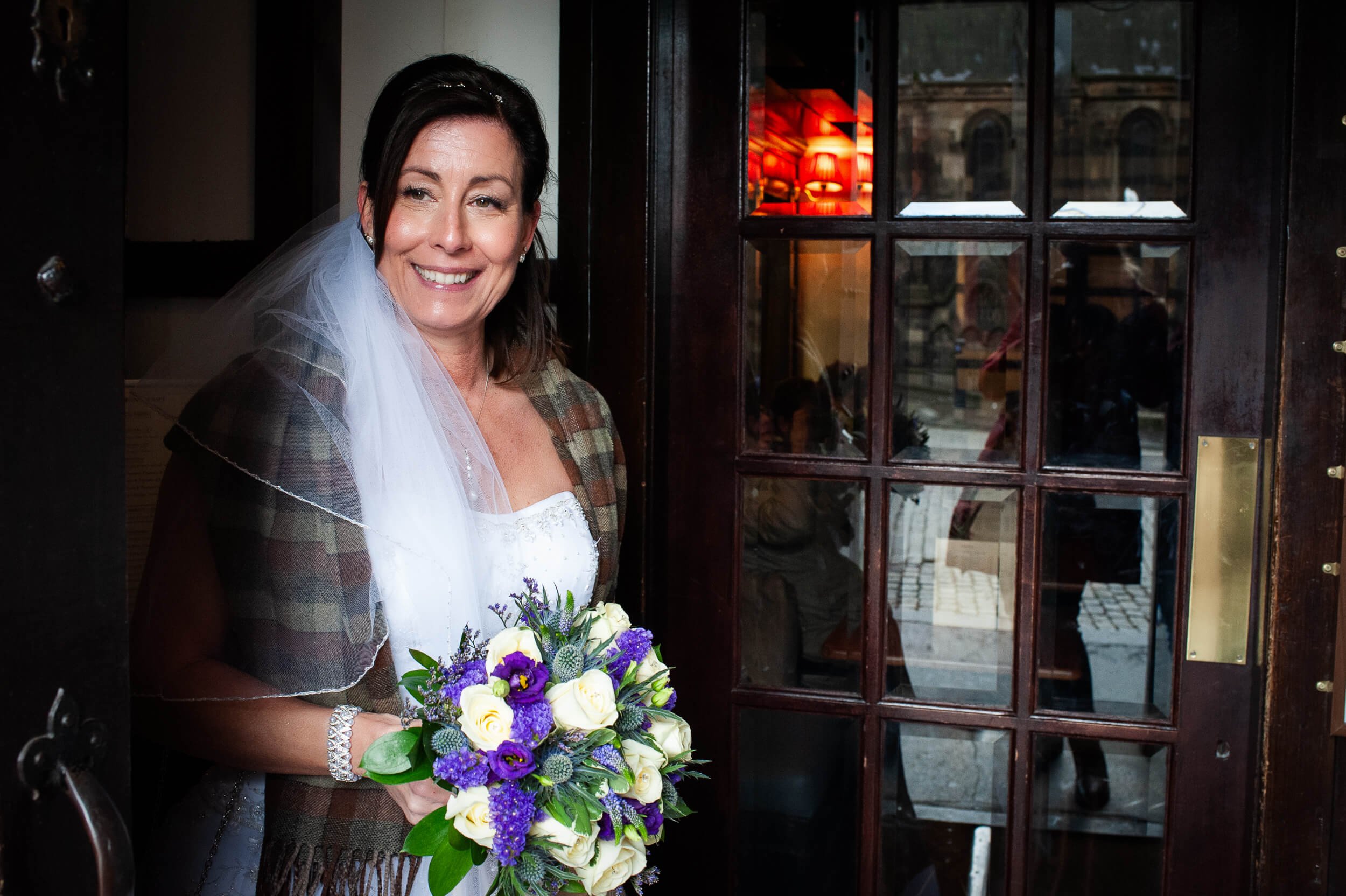 Bride with Scottish tartan shawl and bouquet entering Edinburgh pub after wedding — documentary wedding photography Scotland
