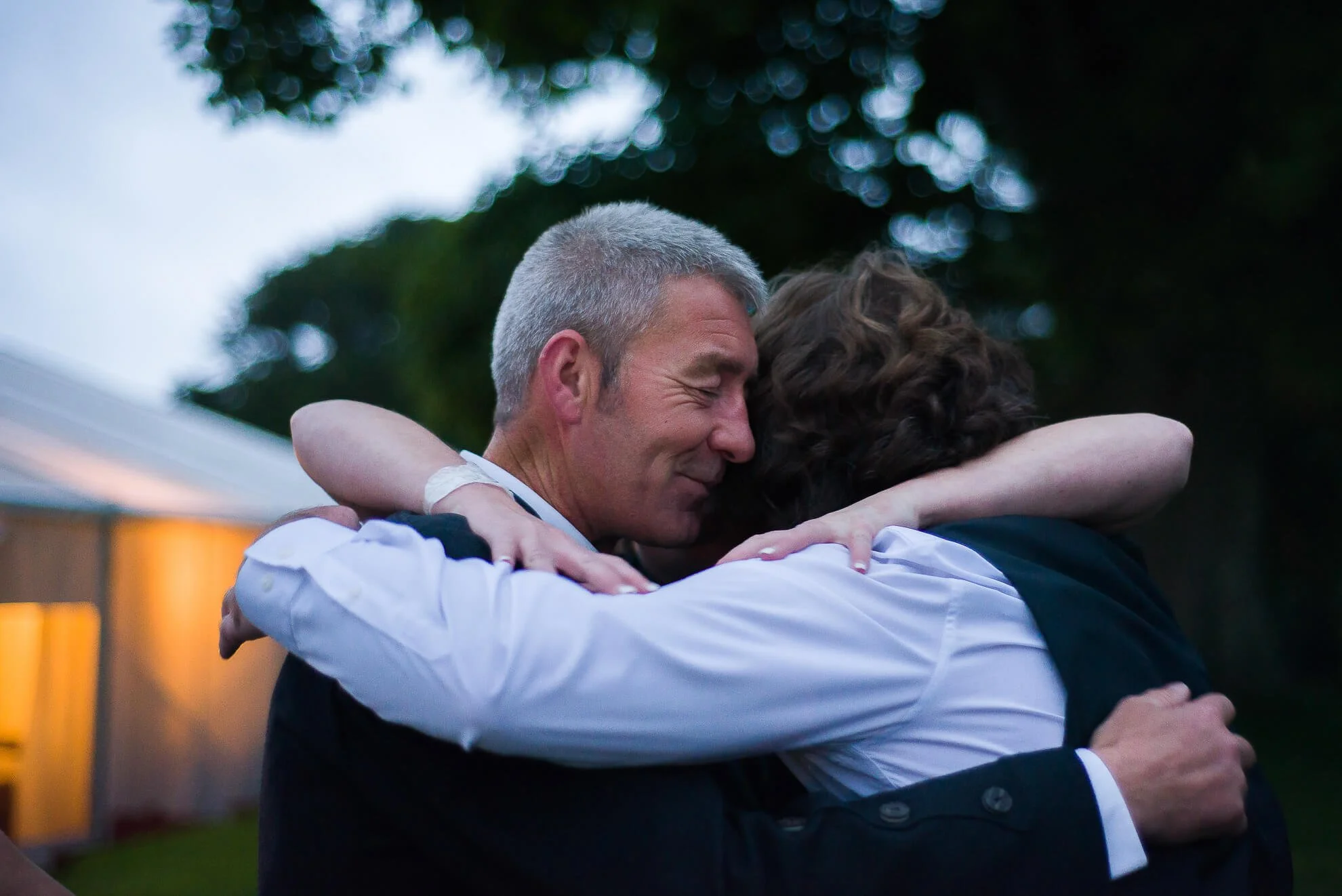 Two people hugging outdoors during evening, with relaxed expressions, demonstrating warmth and connection.