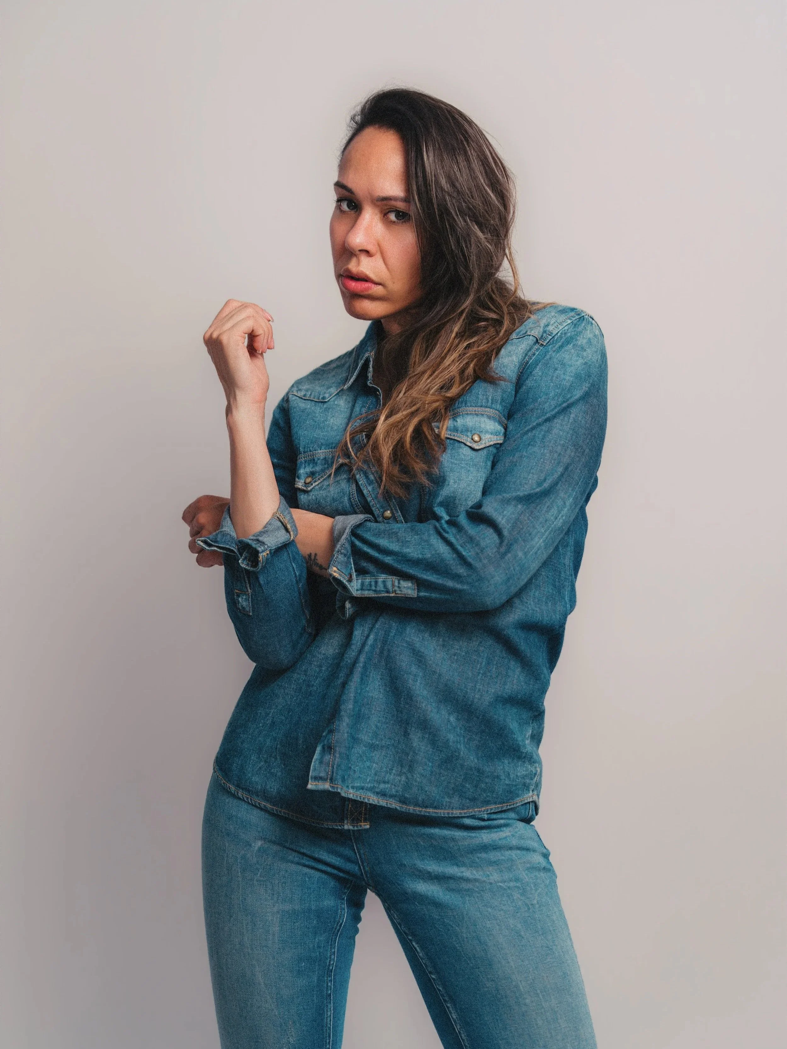 Une mannequin porte une veste en jean et un pantalon en jean, se tenant contre un mur blanc.
