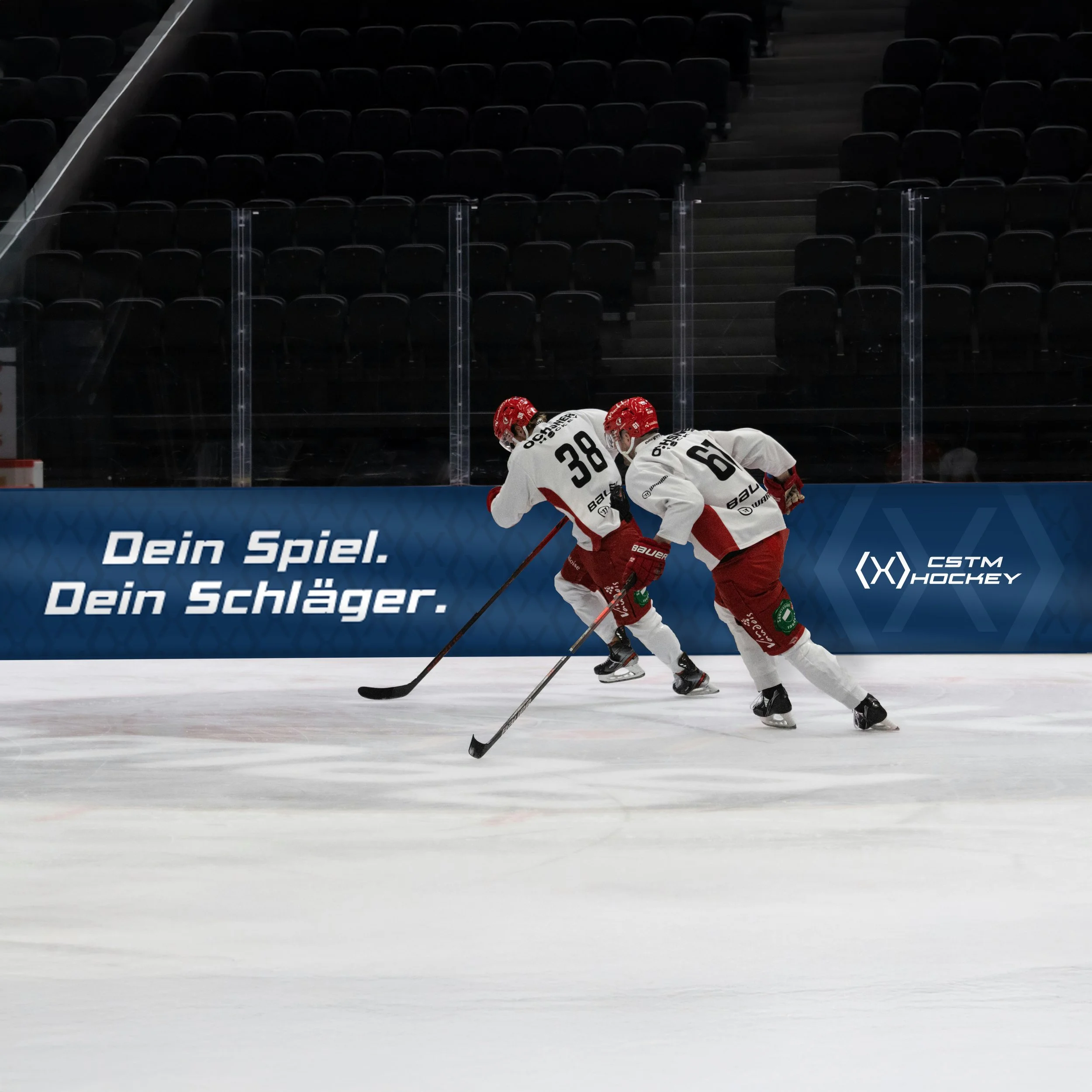 Zwei Eishockeyspieler mit weißen und roten Trikots beim Training auf dem Spielfeld. Eine Werbebande bzw. Werbebanner mit Text und Logo im Hintergrund.