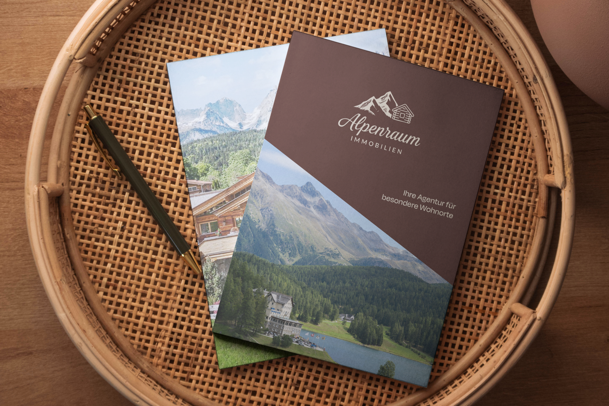 Broschüre für Alpenimmobilien auf einem Rattan-Teller mit einem schwarzen und goldenen Kugelschreiber