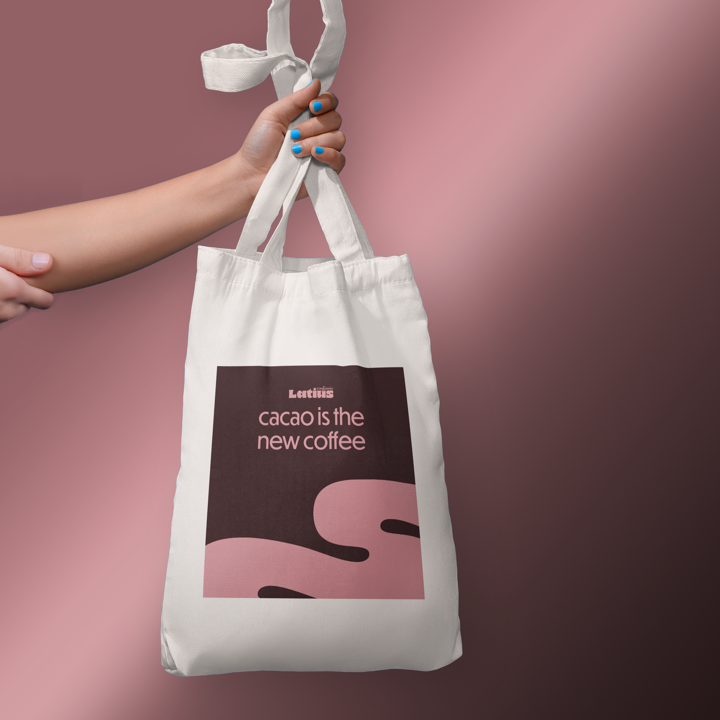 Hand hält einen weißen Designer Stoffbeutel bzw. Jutebeutel mit einem pink-schwarzen Design, das den Text "cacao is the new coffee" enthält, vor einem rosa Hintergrund.