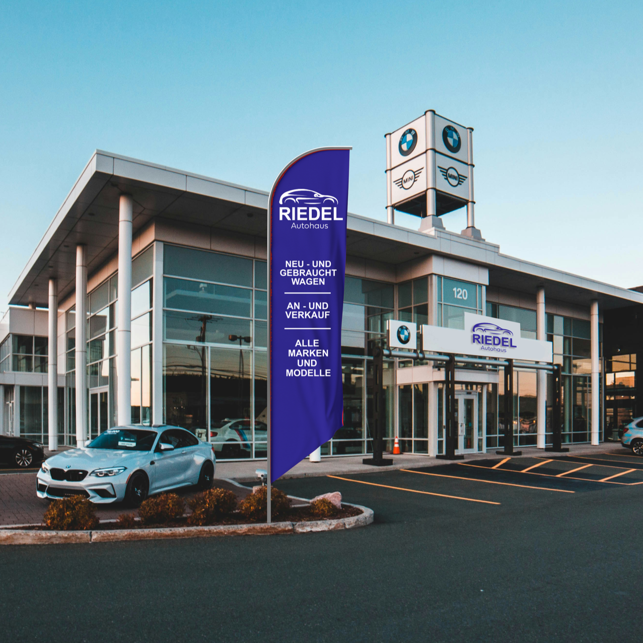 Autohaus Riedel mit BMW und MINI Logos, blaues Verkaufsbanner, einige Autos vor dem Gebäude, Parkplätze, klarer Himmel.