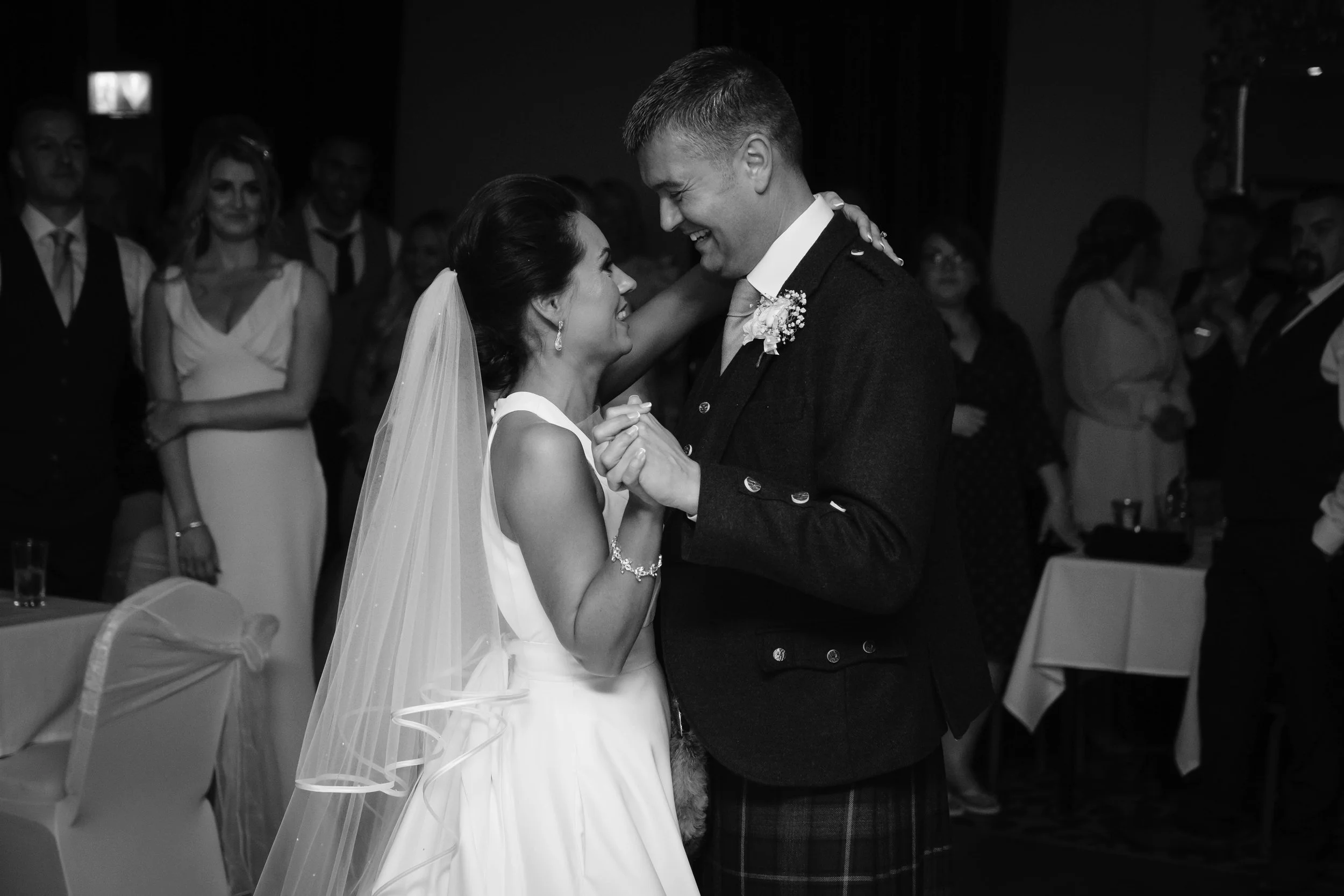 A bride and groom sharing a dance at their wedding reception, surrounded by guests.