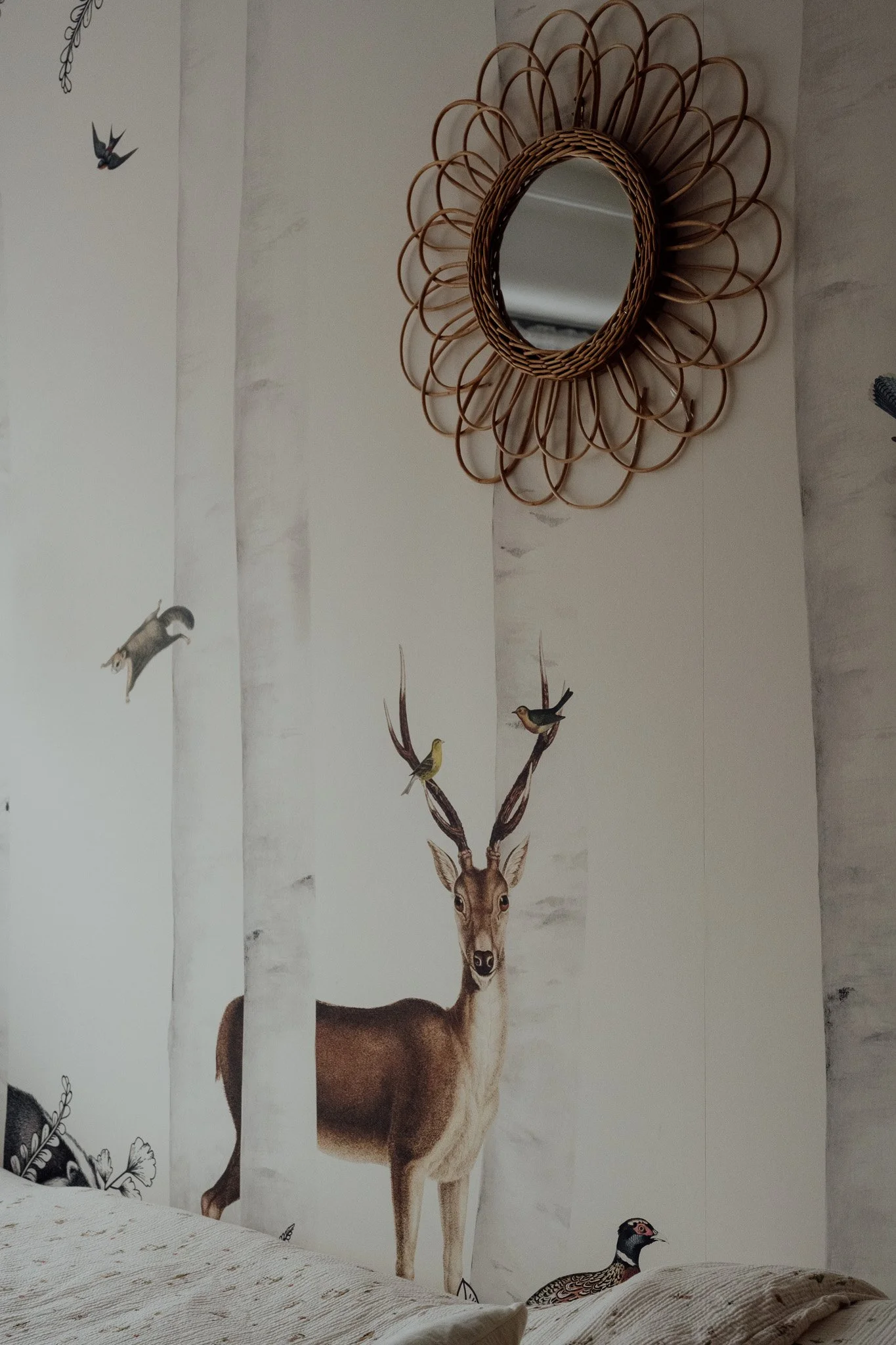 Mur avec décoration de faons, oiseaux et plantes, et miroir en rotin.
