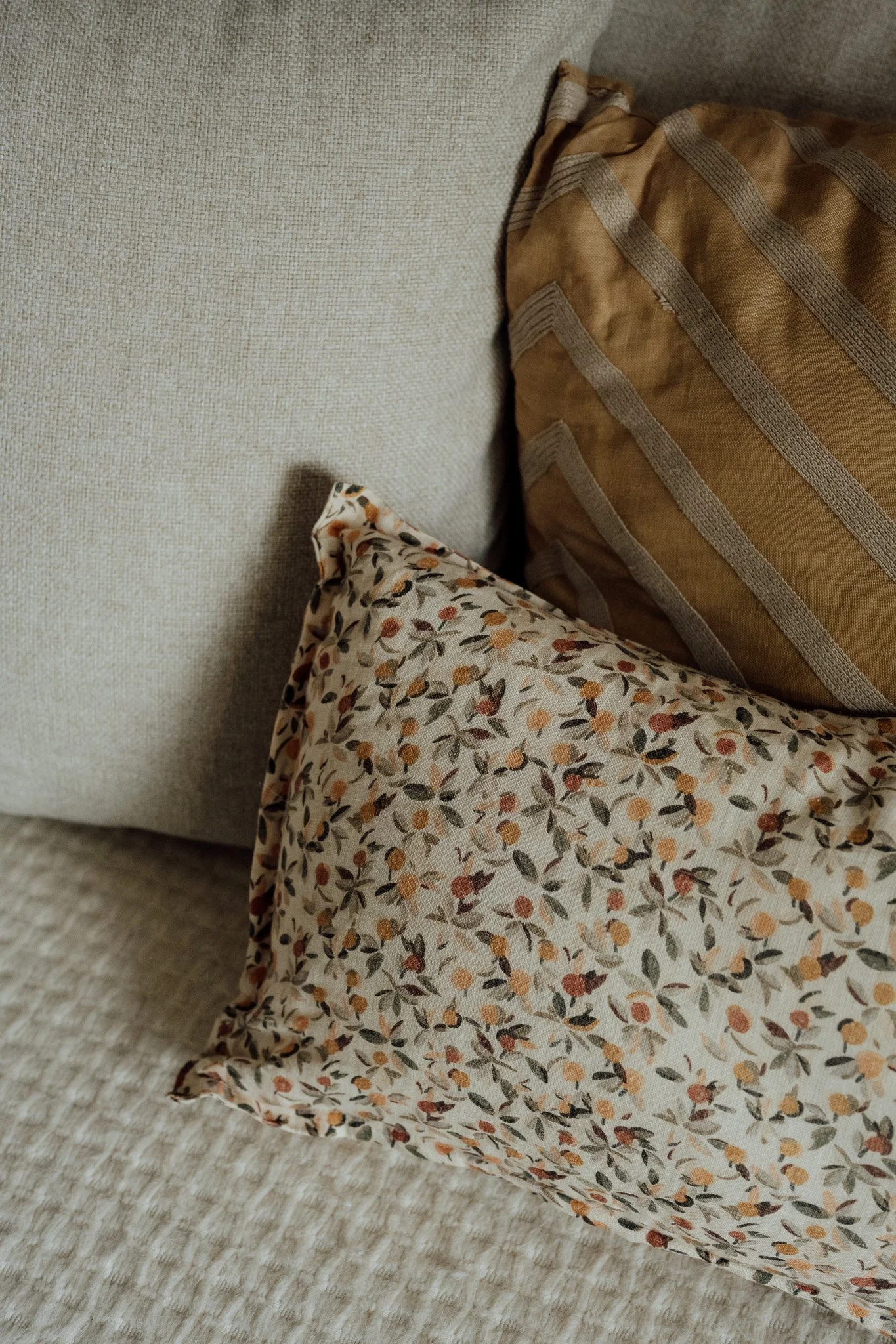 Une vue partielle d'une pièce avec un canapé clair, un coussin beige avec des rayures, et une jupe ou une robe à motifs floraux aux couleurs chaudes à l'avant.