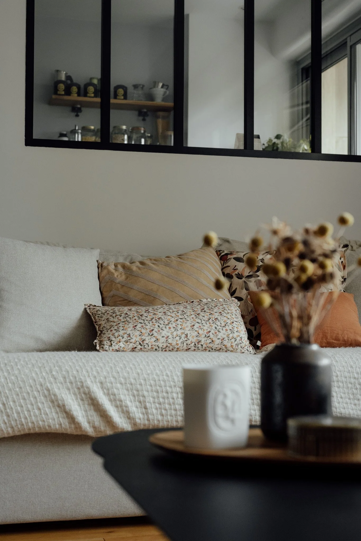 Un canapé beige avec plusieurs coussins de différentes tailles, motifs et couleurs, dans un salon élégant.