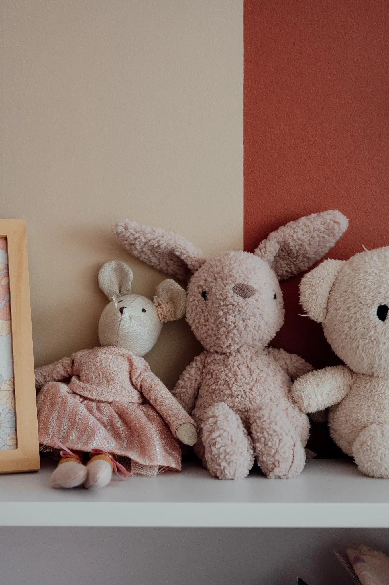 Une étagère avec des peluches roses et une statuette de lapin, contre un mur bicolore beige et rouge.