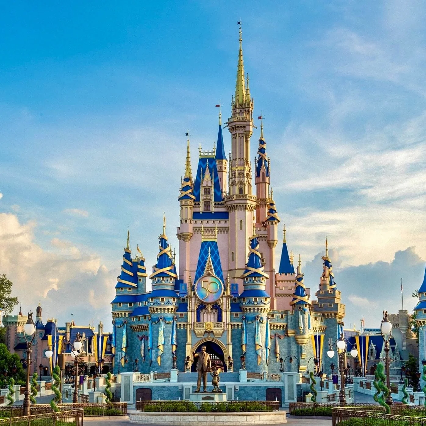 Disney castle with blue and pink turrets, celebrating its 50th anniversary, under a partly cloudy sky.