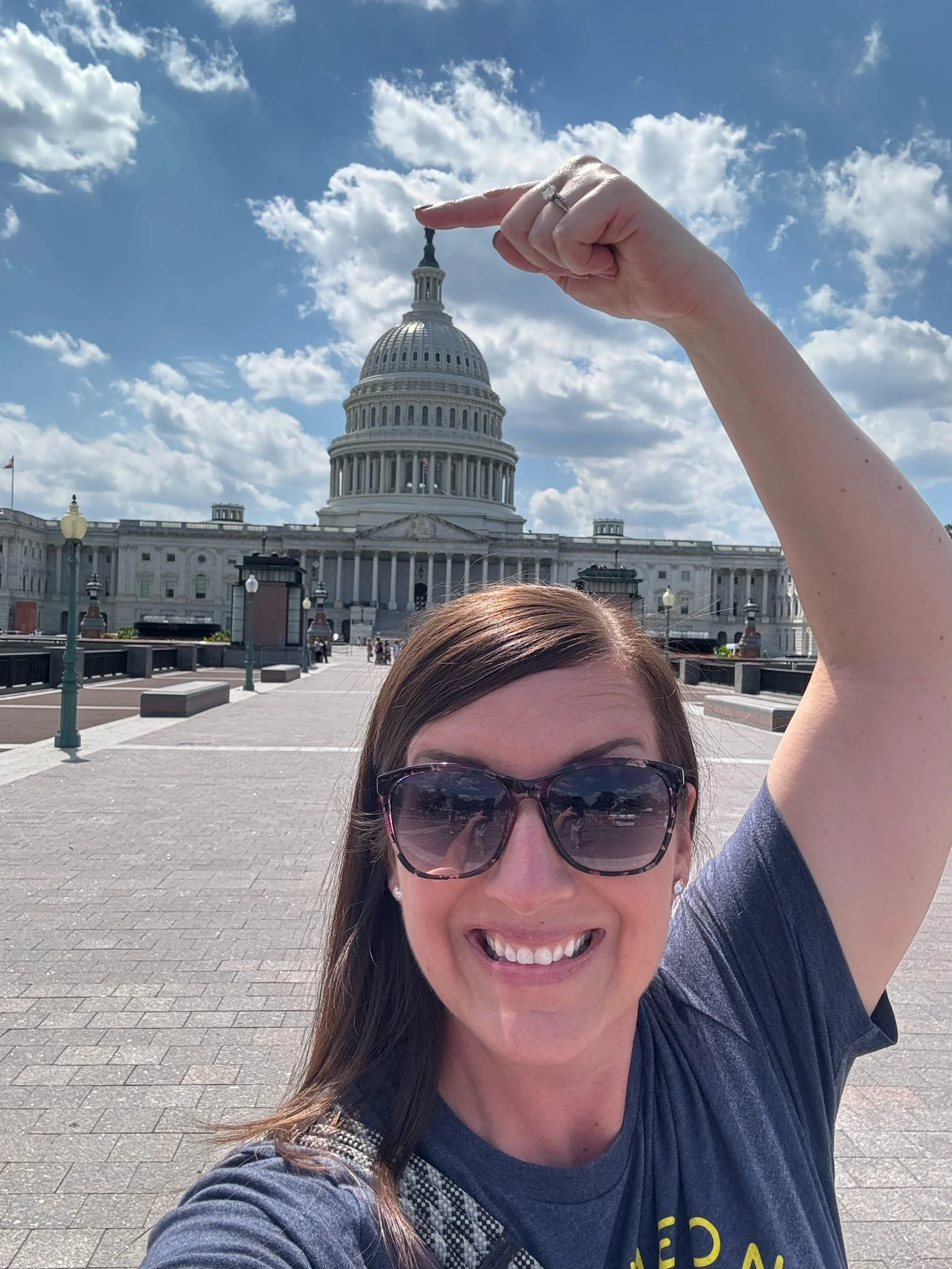 Woman smiling, wearing sunglasses, taking a selfie in front of the U.S. Capitol building in Washington, D.C.
