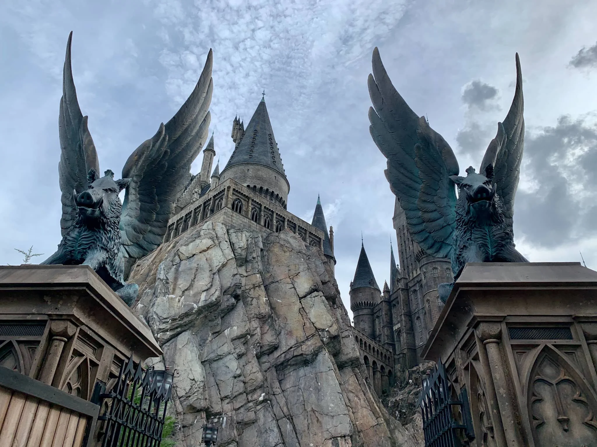 A woman with sunglasses taking a selfie in front of a castle at a theme park, with blue sky and sunlight.