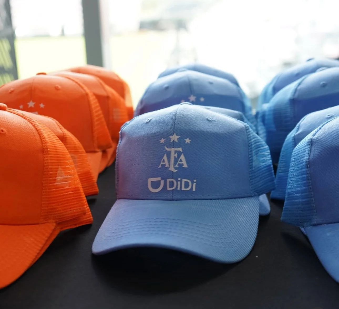 Multiple blue and orange baseball caps with logos, displayed on a table near a window.