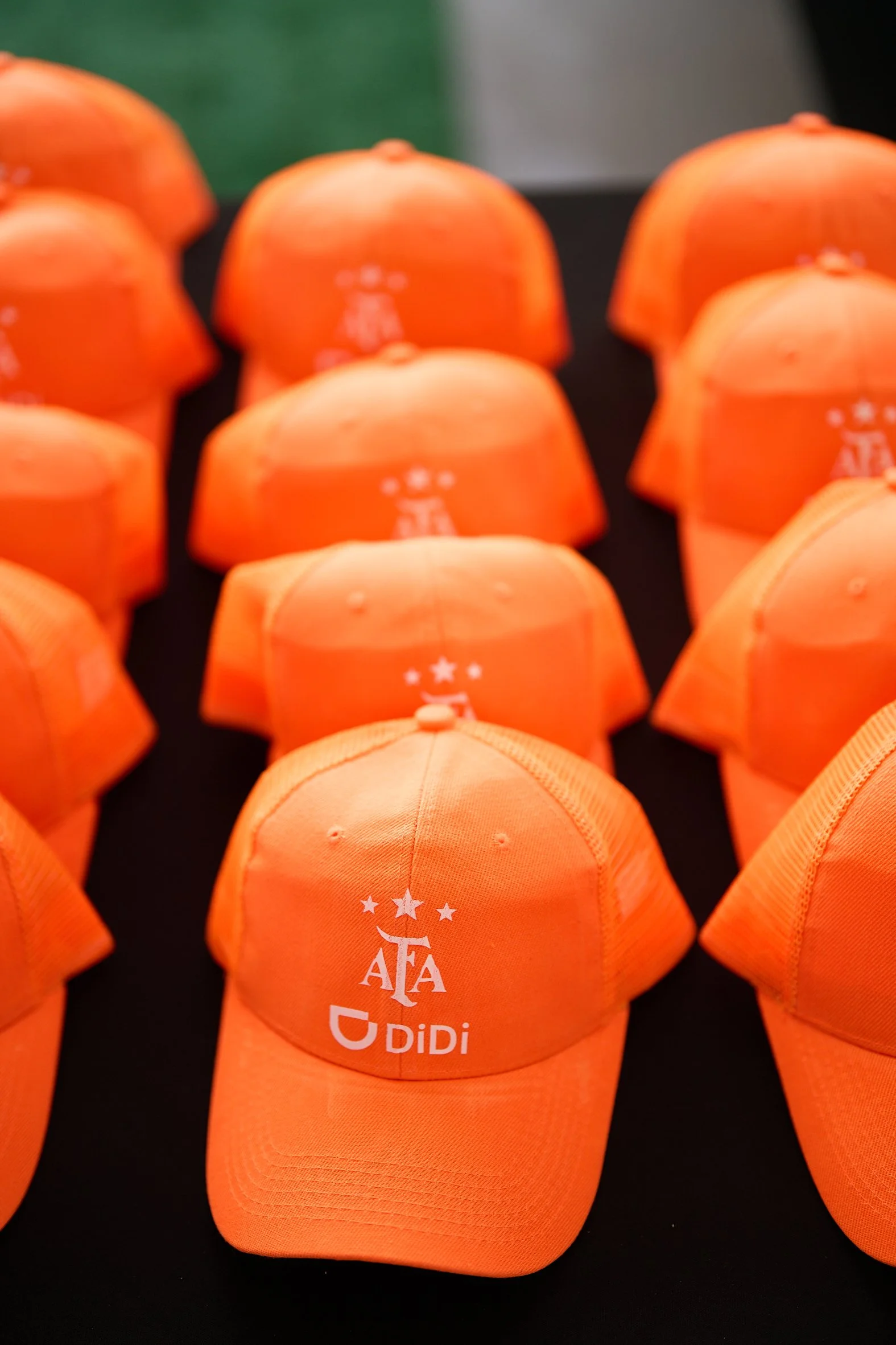Multiple orange caps with the logo of the American Football Association (AFA) and sponsor Didi printed on the front, arranged on a black surface.