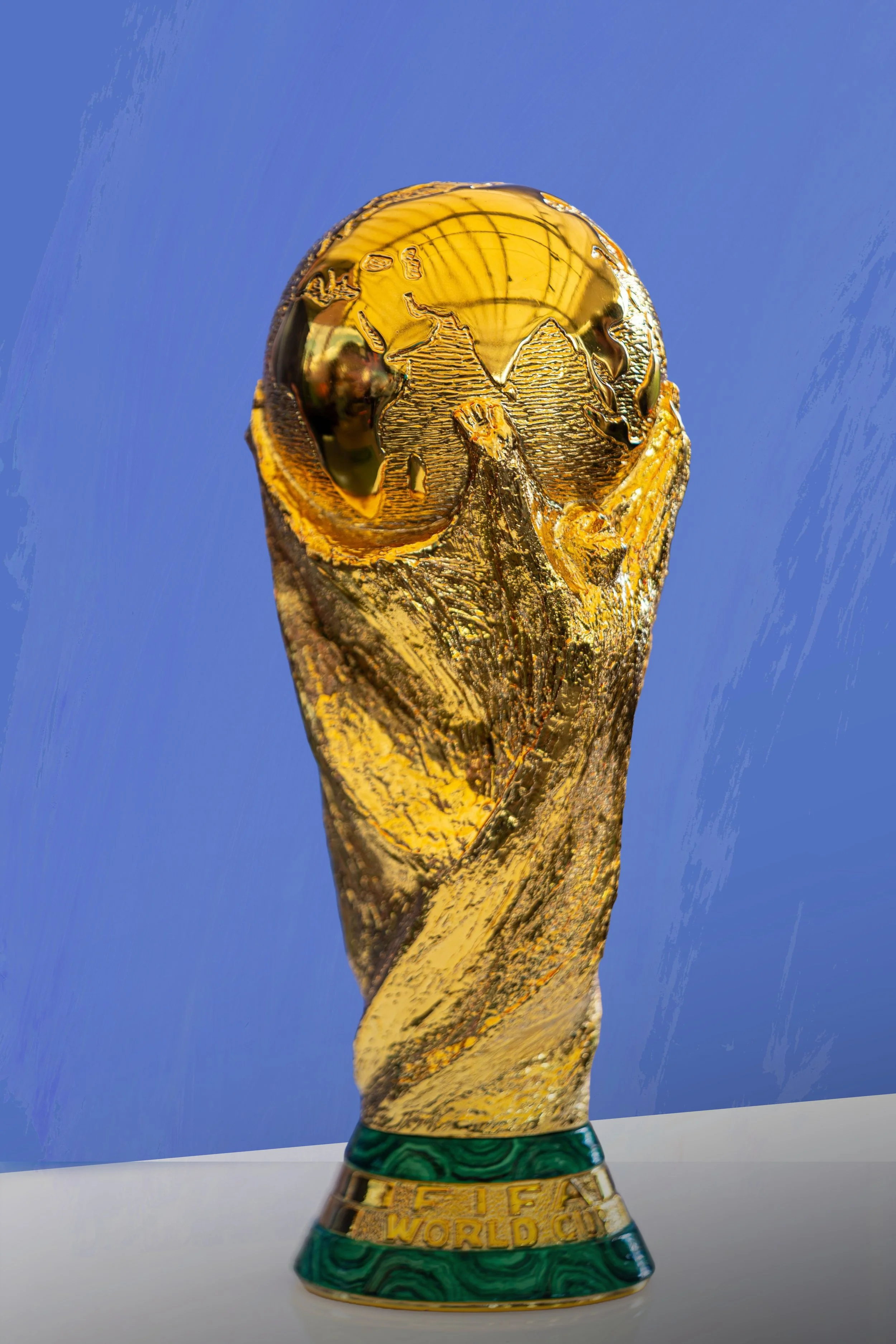 The FIFA World Cup trophy, gold with green base, against a blue background.