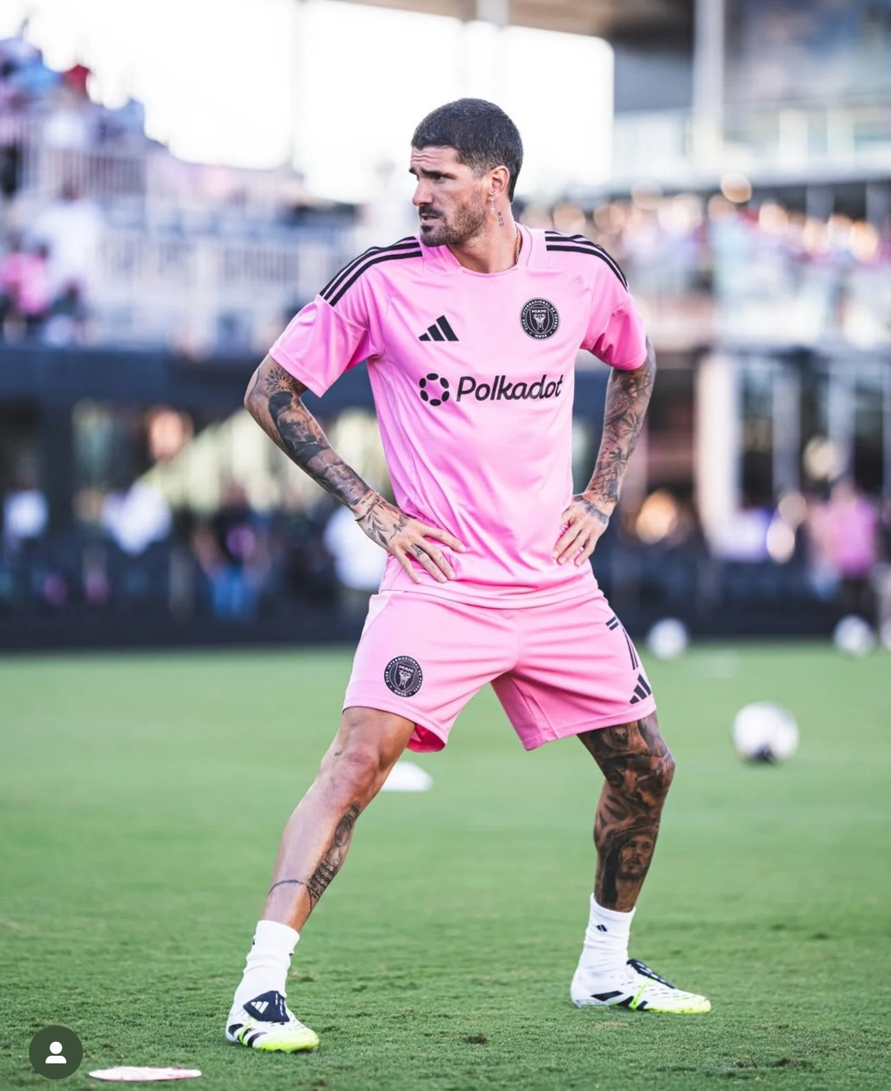 A male soccer player in a pink uniform standing on a soccer field, with hands on hips, during training or practice.