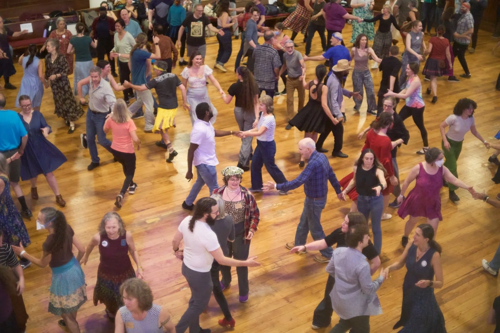 People dancing at a crowded social event on a wooden floor in a community hall.
