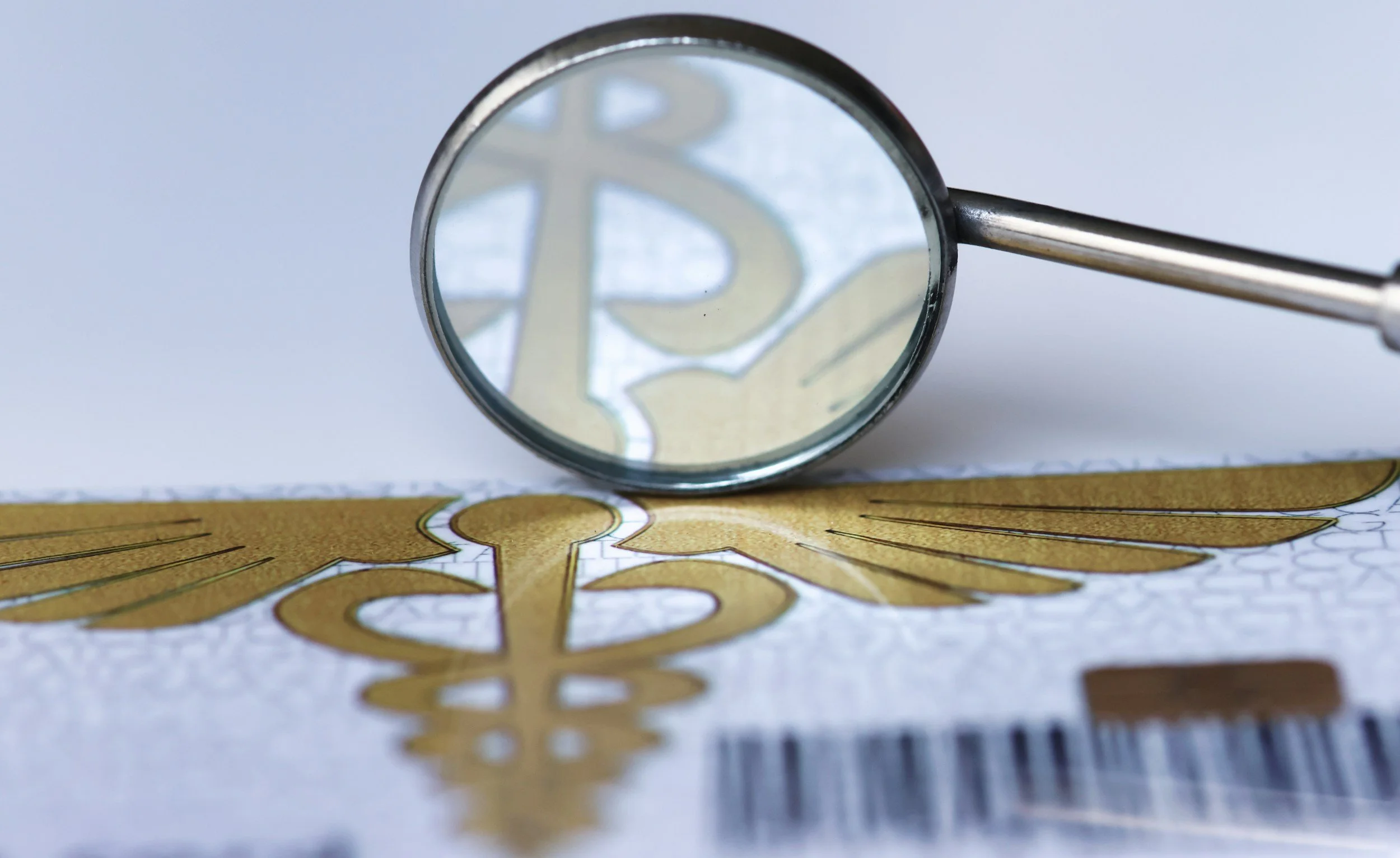 Close-up of a magnifying glass focusing on a gold-colored dollar sign and wing symbol on a banknote.