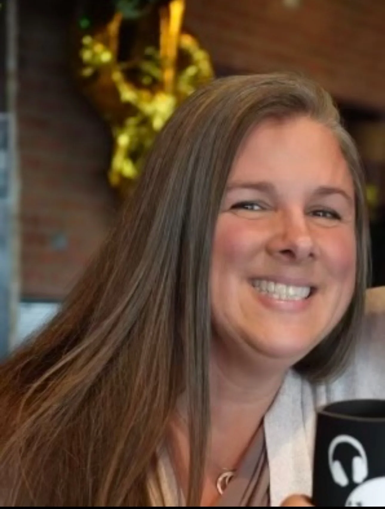 A woman with long brown hair smiling while holding a microphone, with a gold balloon shaped like a number in the background.