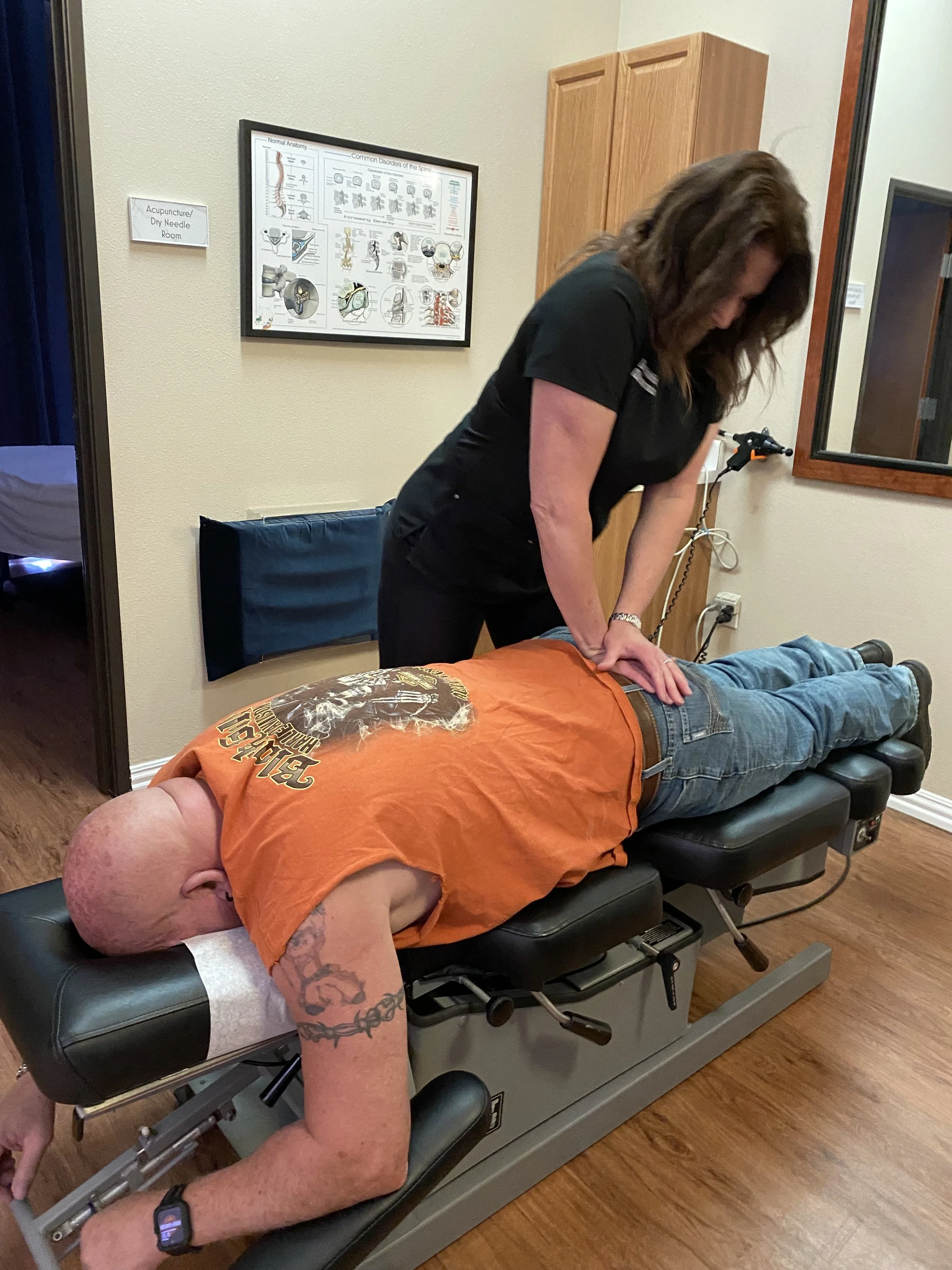 A chiropractor or medical professional performs an adjustment on a patient lying face down on a chiropractic table in an examination room.