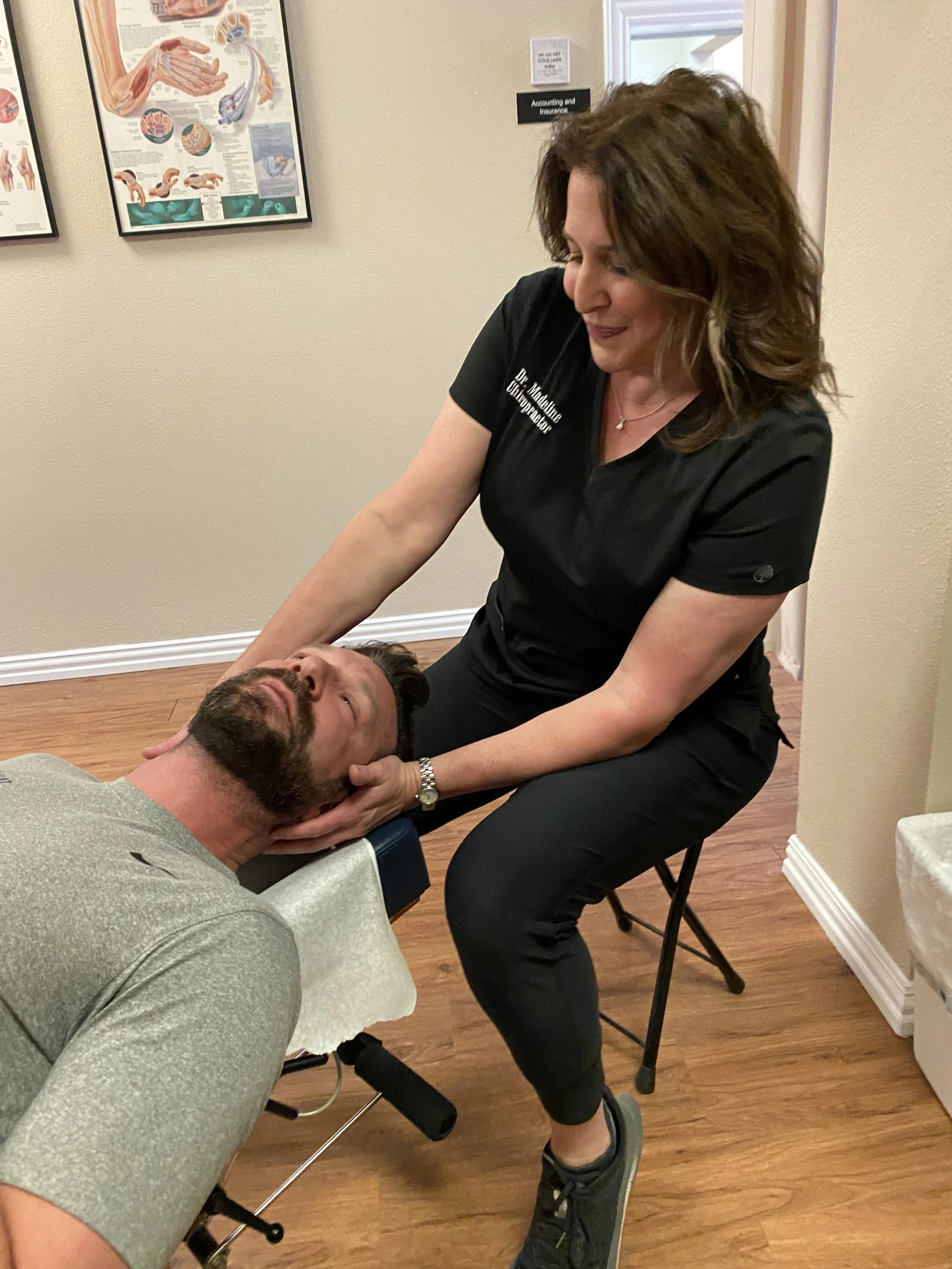 A woman providing chiropractic care to a man lying on a chiropractic table in an office.