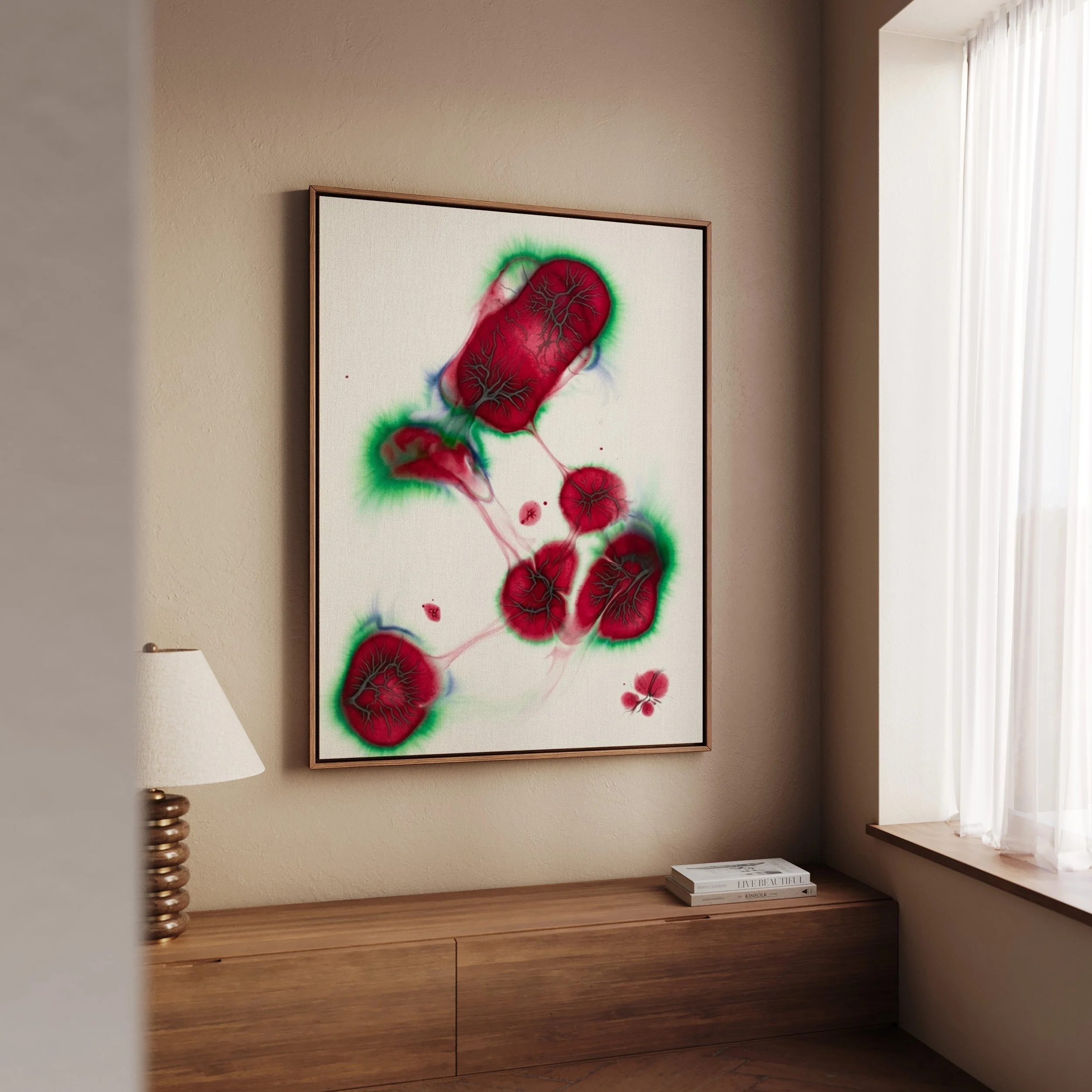 A framed abstract artwork with red, black, and green colors hangs on a beige wall in a room with wooden furniture, a white lamp, and a window with sheer white curtains.