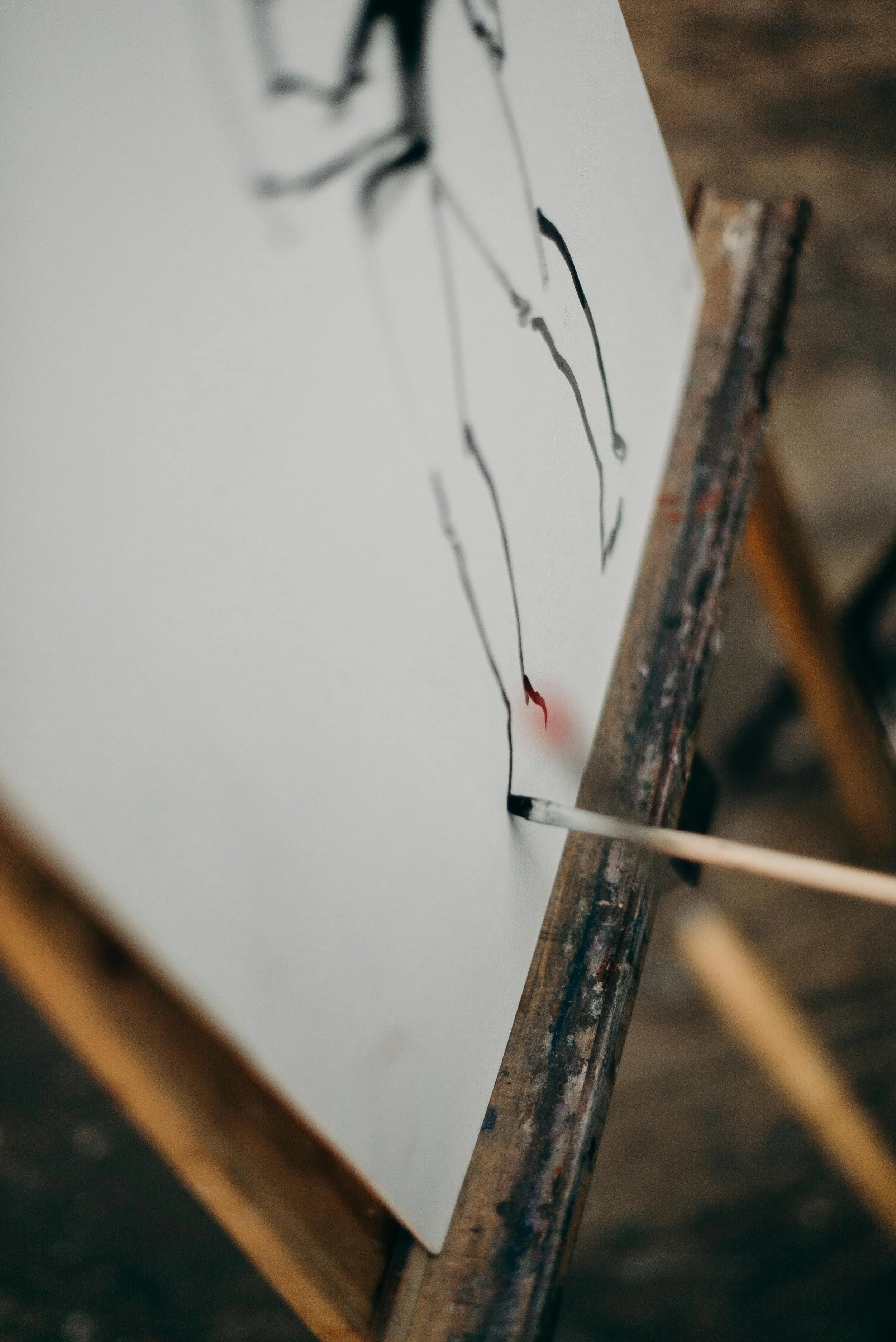 Close-up of a white canvas with black and red abstract ink painting, leaning against a rustic wooden surface.
