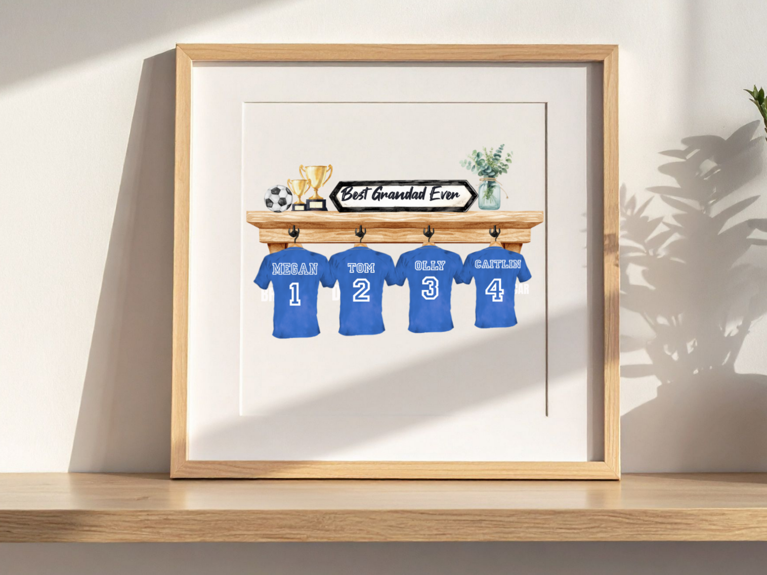 Decorative wall art featuring a wooden shelf with four blue jerseys labeled with names and numbers, trophies, a soccer ball, a sign reading 'Best Grandad Ever,' and a plant in a glass jar.