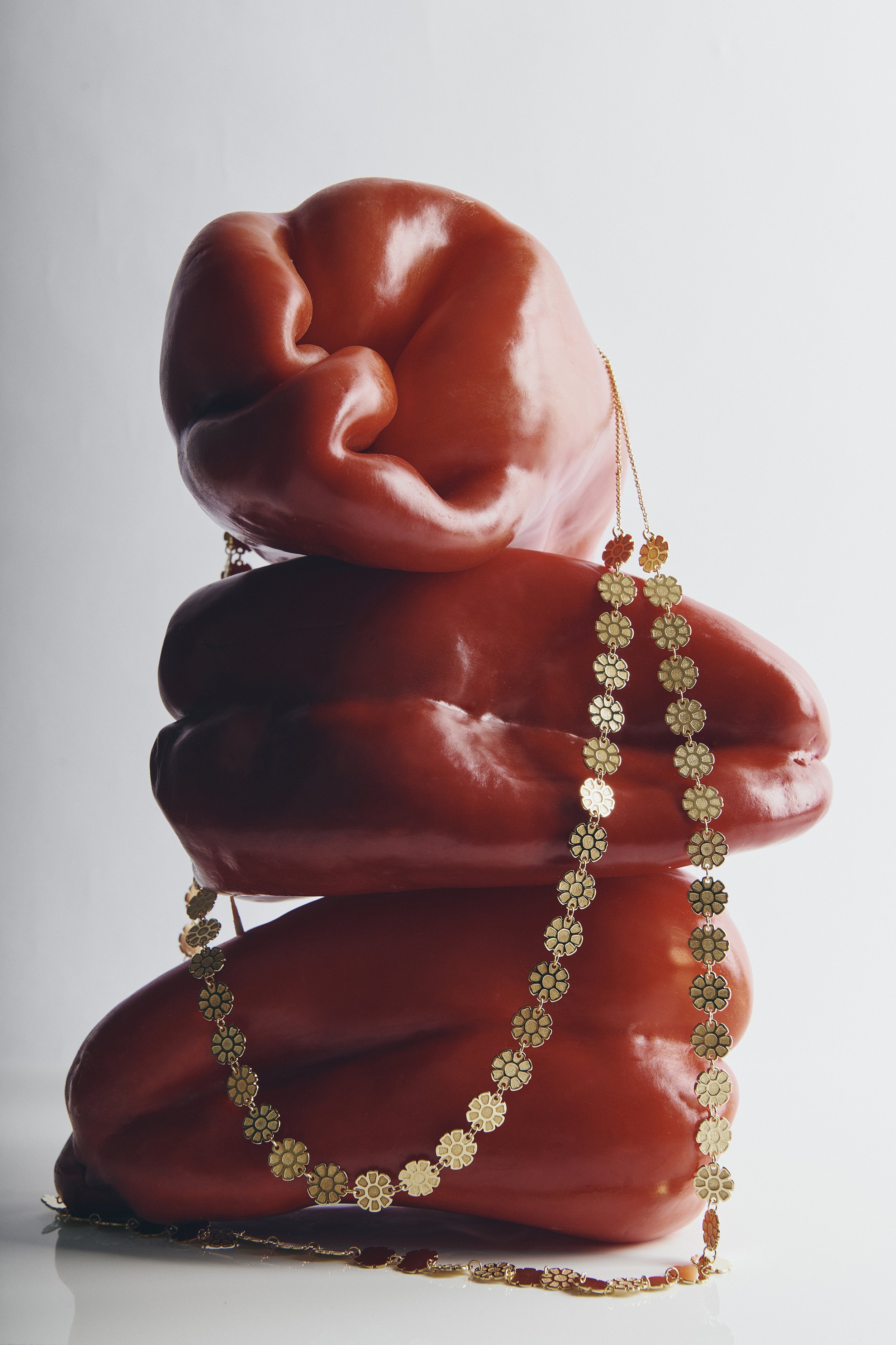 Stacked red peppers with gold flower-shaped necklaces draped over them.