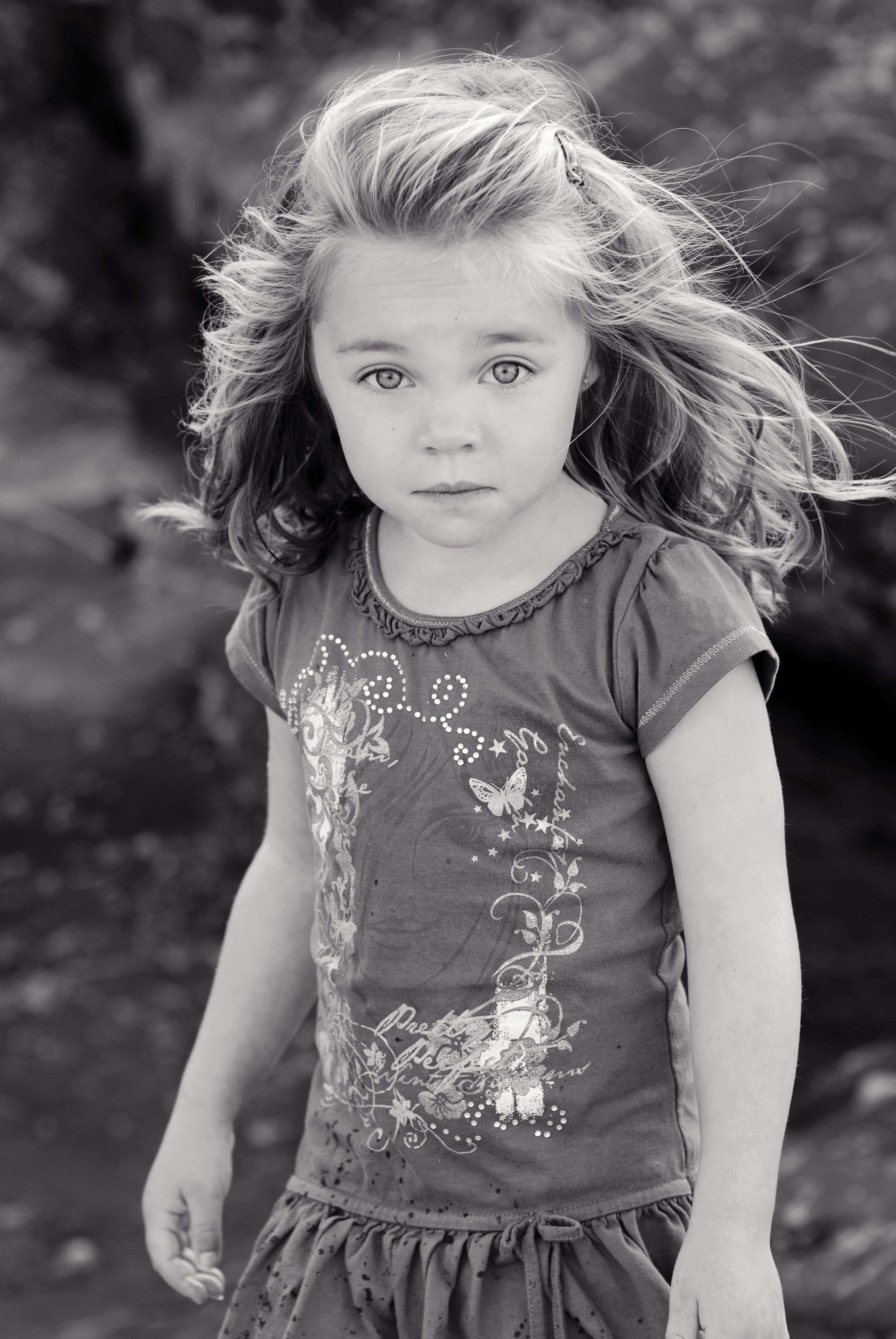 A young girl with long, wavy hair looking directly at the camera outdoors.