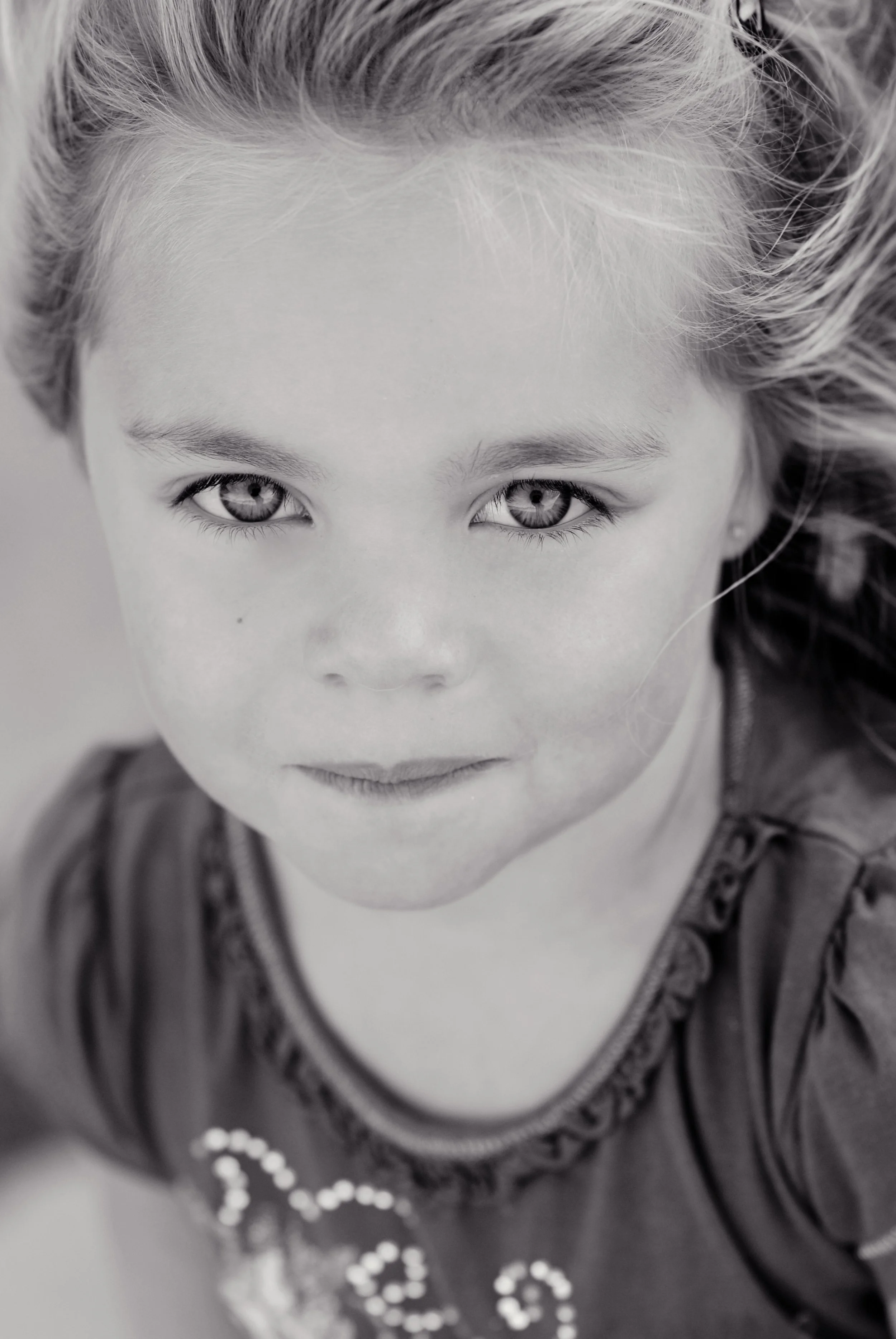 Close-up black-and-white portrait of a young girl with striking eyes and wavy hair, looking directly at the camera.