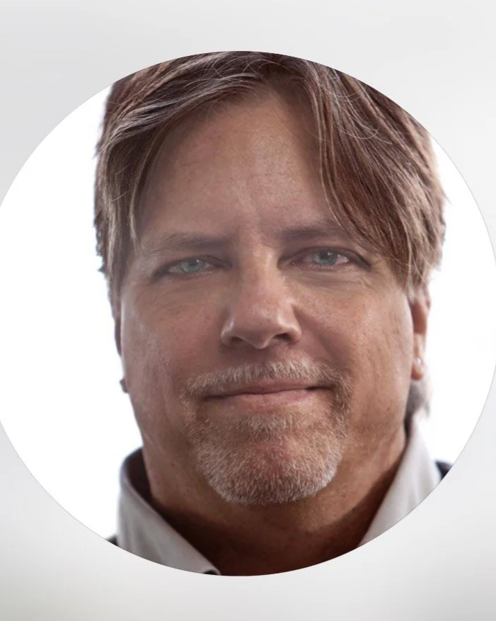 Close-up portrait of a middle-aged man with light brown hair, blue eyes, and a beard, wearing a collared shirt.