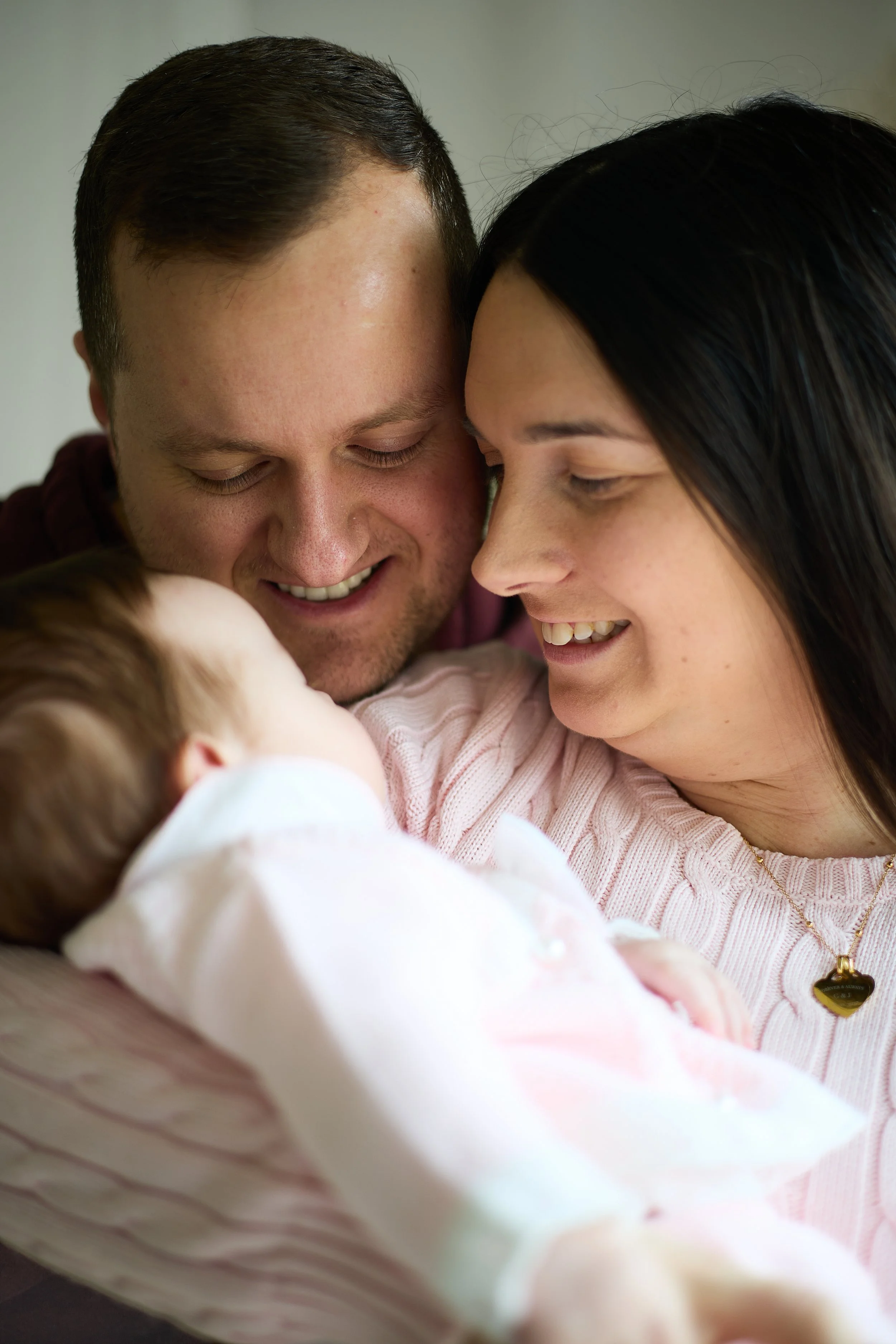 A happy family moment with a man, woman, and newborn baby. The parents are smiling and looking at their baby, who is lying in the woman's arms.