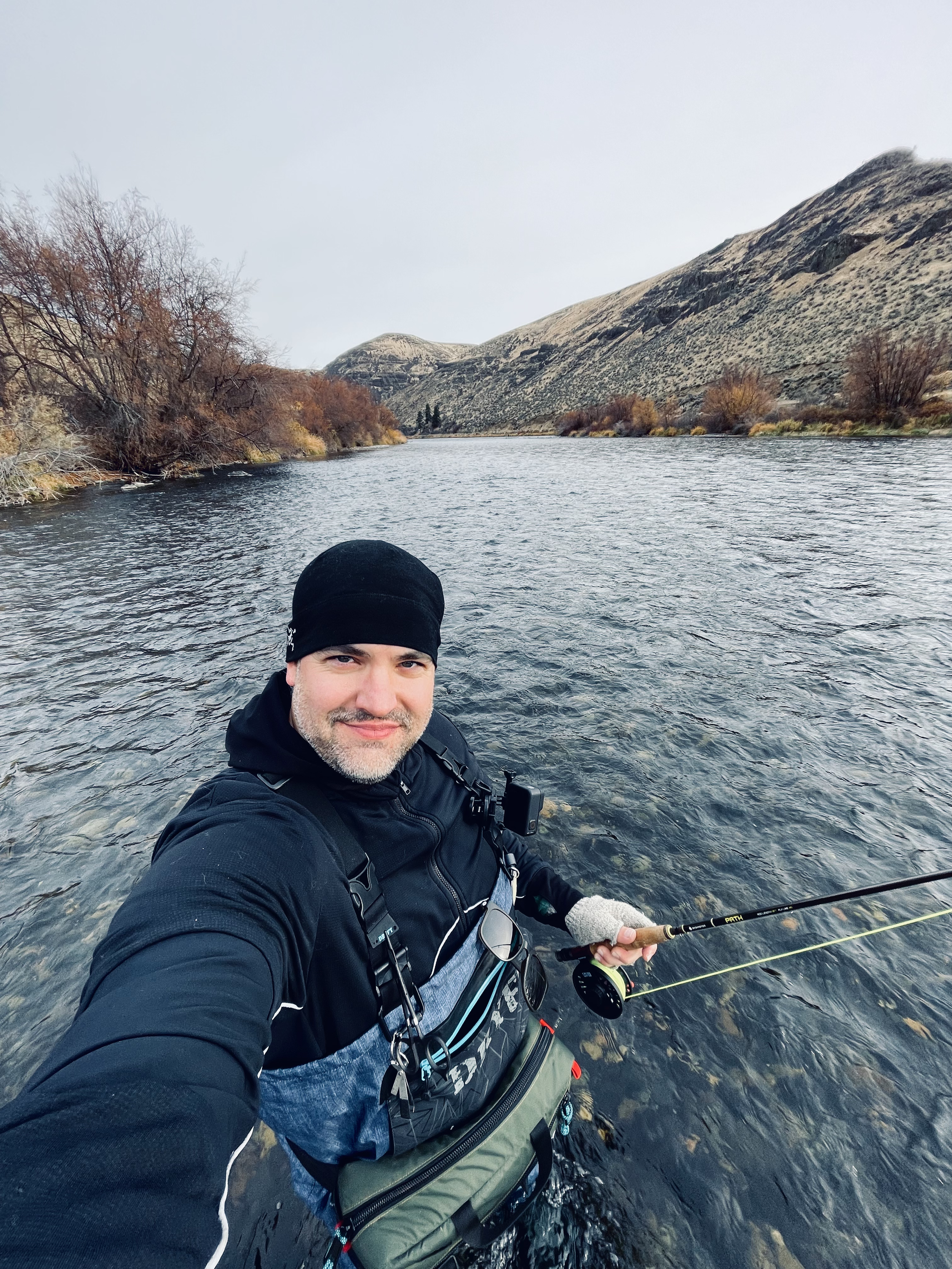 Tim not working and outside standing in a river acting like a fisherman.