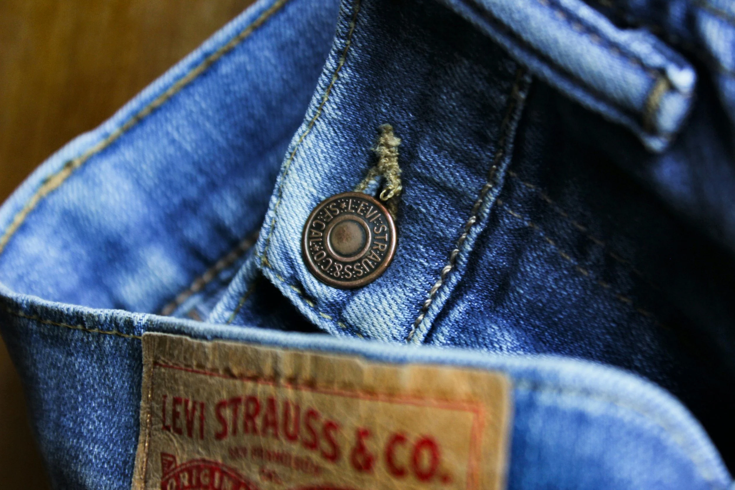 Close-up of a blue denim Levi's jeans pocket, showing the metallic button with 'Levi Strauss & Co.' engraved, a part of the red Levi's label, and part of the fabric.
