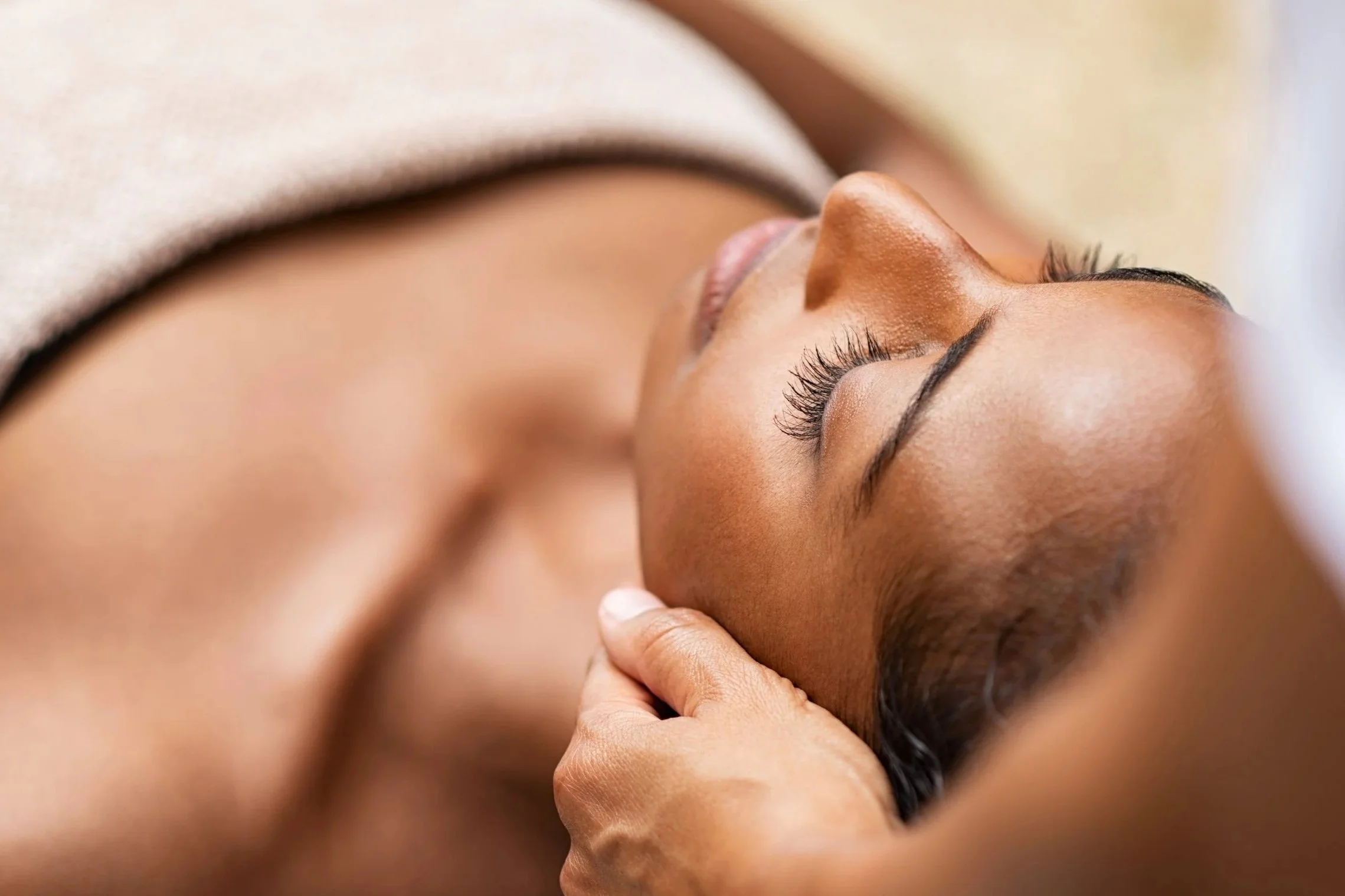 A woman receiving a massage, lying on her back with her eyes closed.