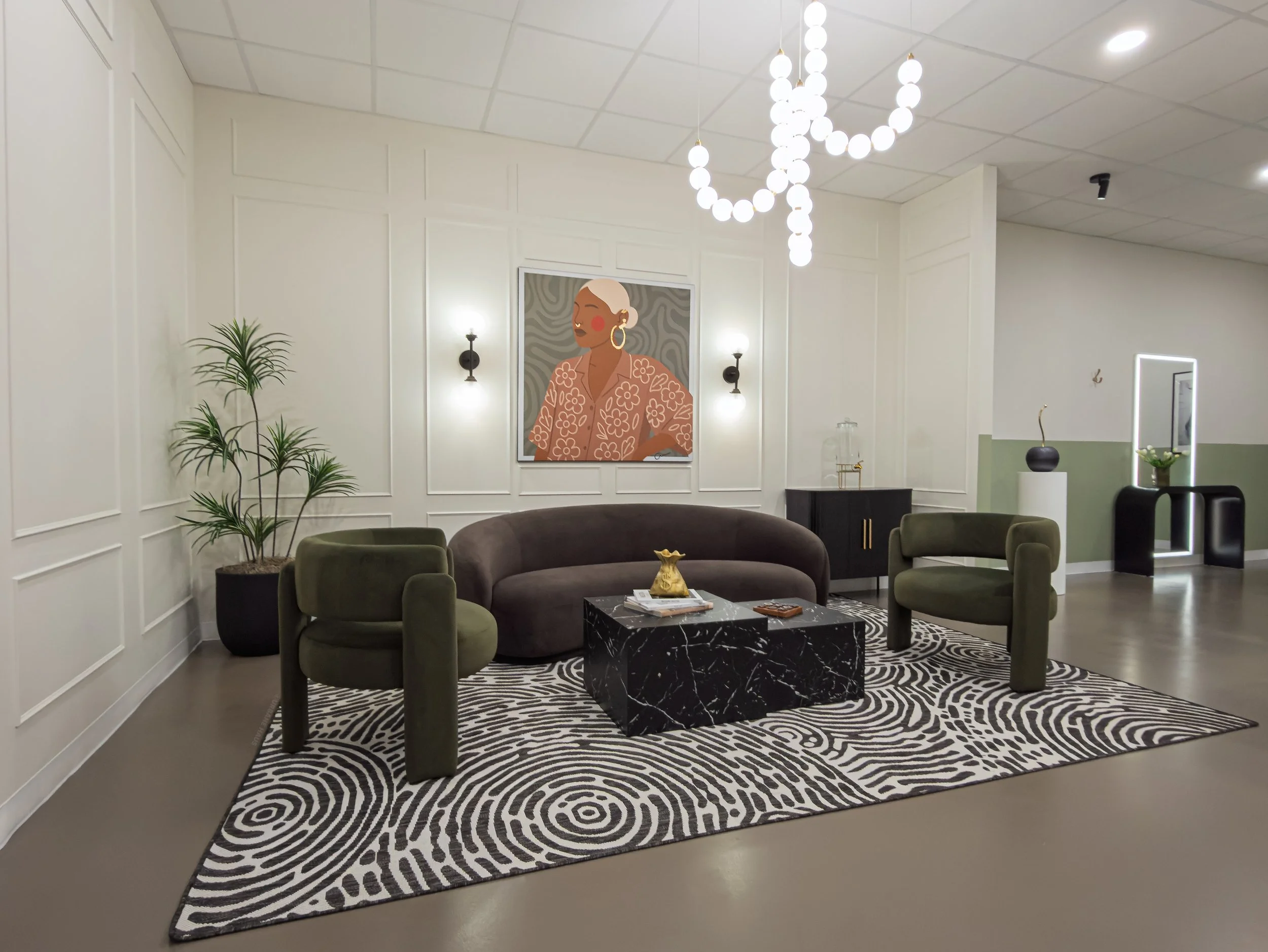 Modern living room with four green armchairs, a brown sofa, a black marble coffee table, a patterned black and white rug, a large colorful artwork of a woman, plants, wall sconces, and a chandelier of round white lights.