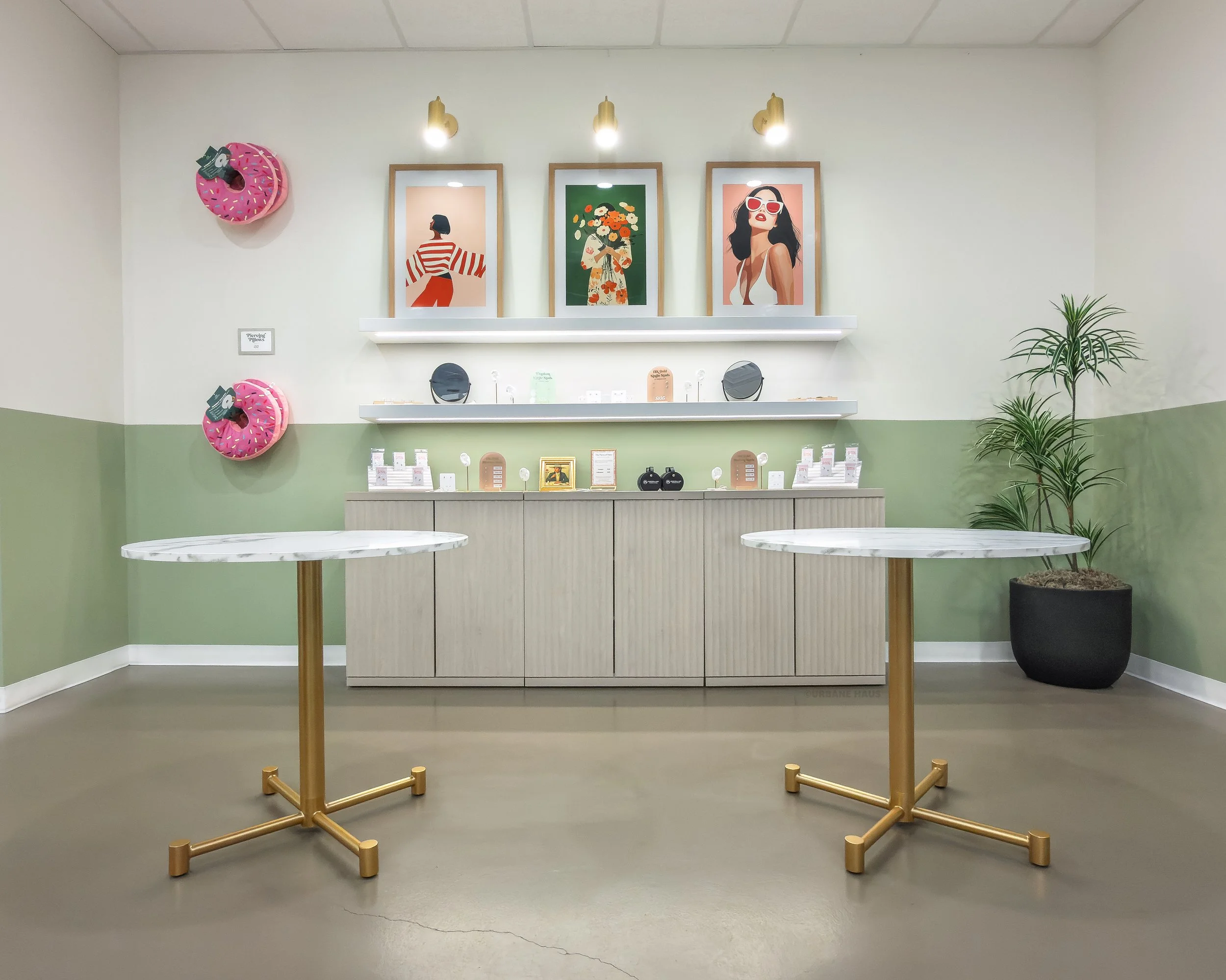 Sweet shop interior with two round marble-topped tables with gold bases, artwork of women on the wall, decorative items, and a potted plant.