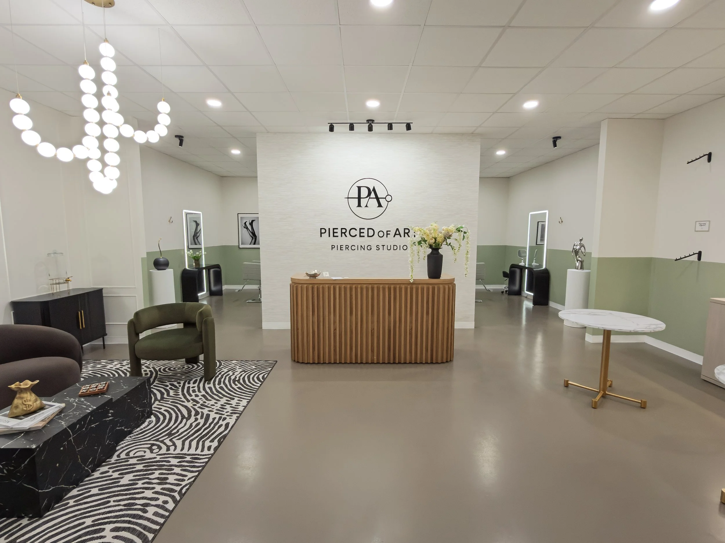 Interior view of Pierced Art piercing studio with minimalist design, featuring a reception desk, modern lighting, decorative artwork, and seating area.