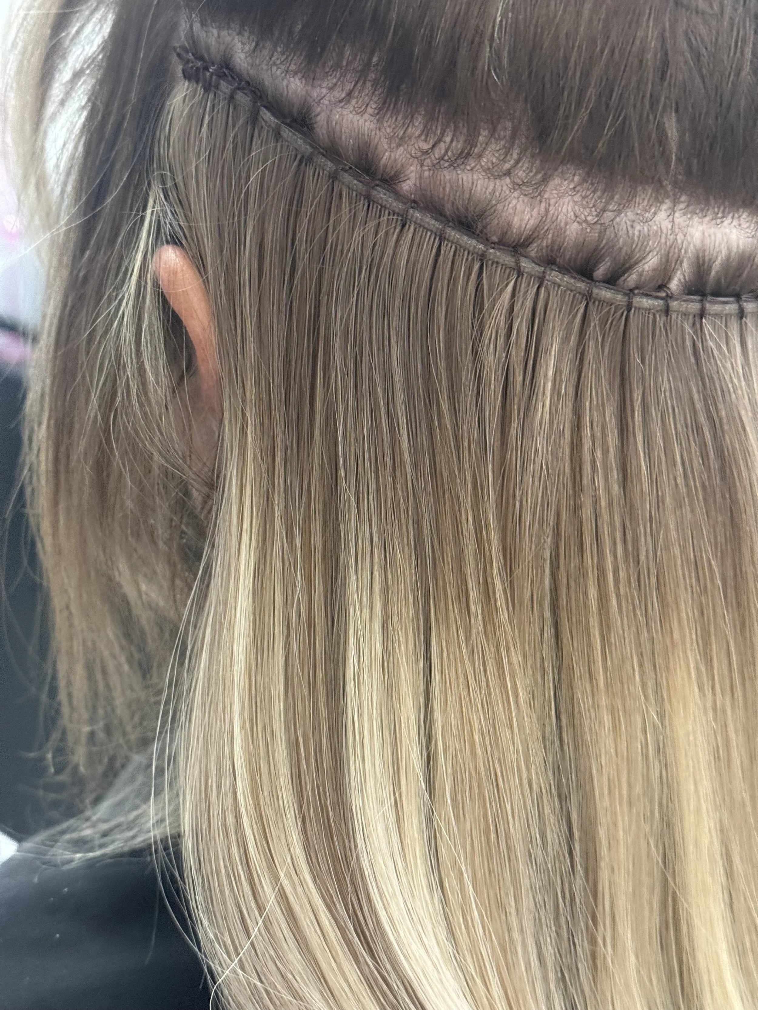 Close-up of a person's head showing their hair putting in hair extensions, with a section of hair lifted to reveal the scalp.