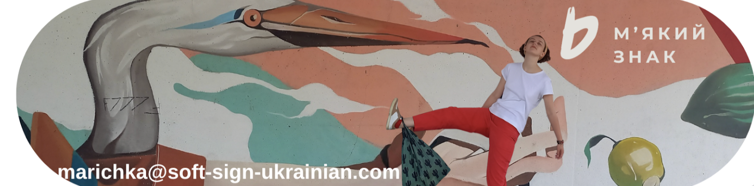 A woman in a white t-shirt and red pants posing in front of a colorful mural wall featuring a large bird and abstract shapes.