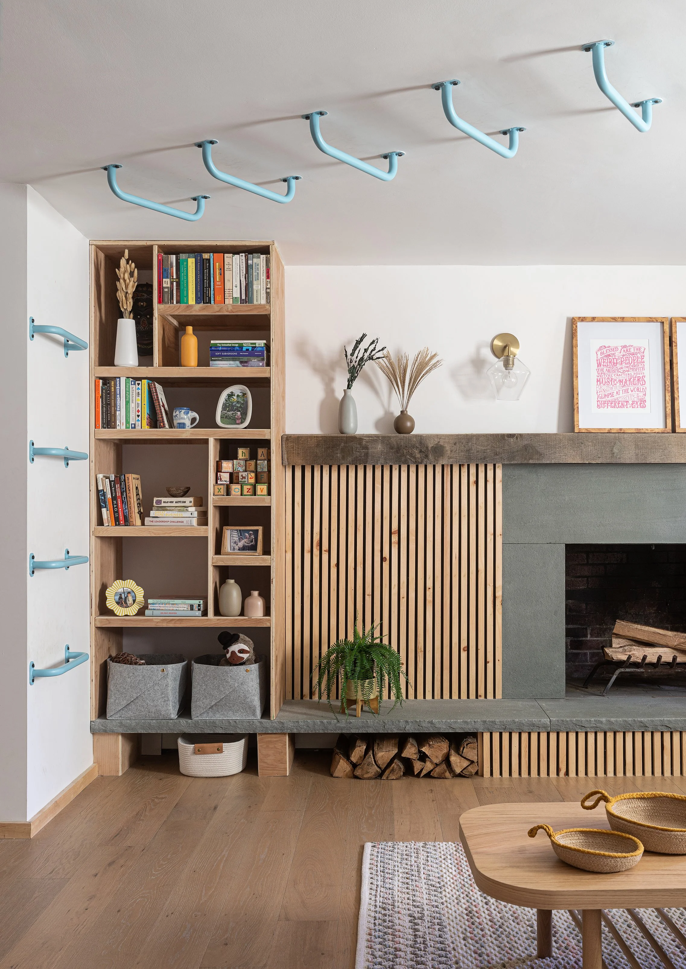 Living room with a wooden fireplace, a bookshelf filled with books and decorative items, a potted plant, and a wall-mounted light fixture.