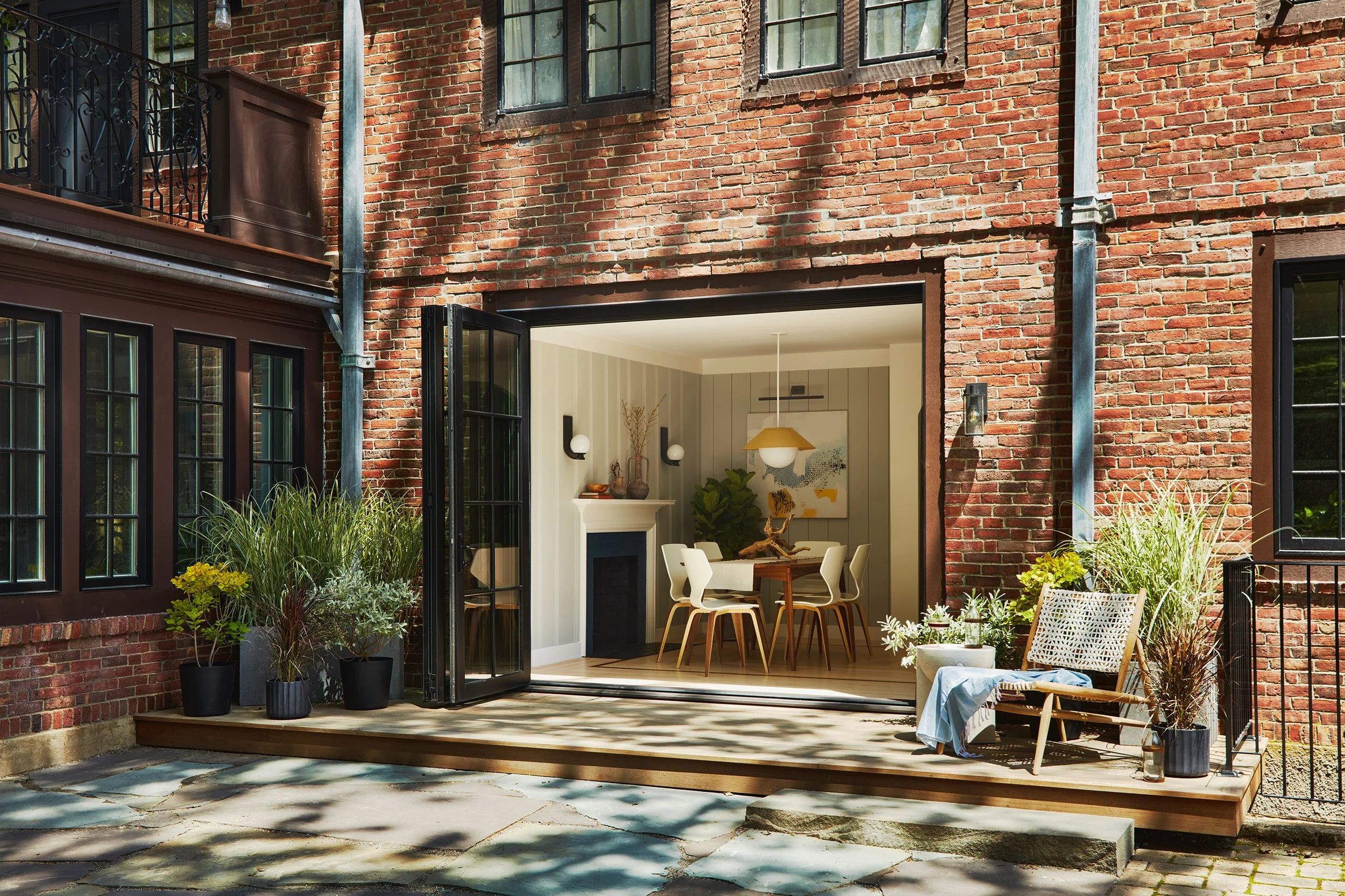 Open patio door leading into a modern dining room in a brick house with outdoor plants and a lounge chair on the patio