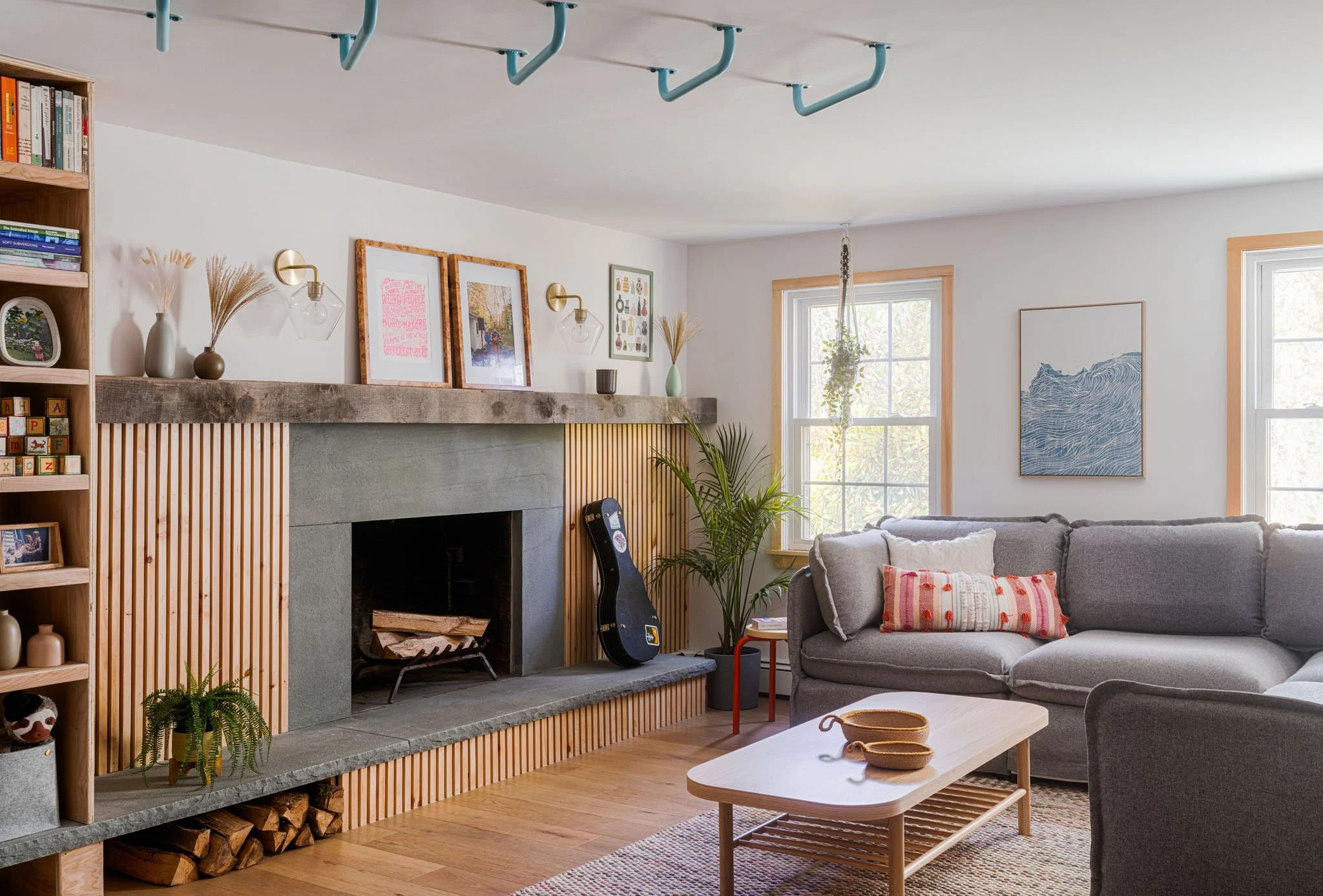 Living room with a fireplace, bookshelf, gray sofa, wooden coffee table, plants, and wall art.