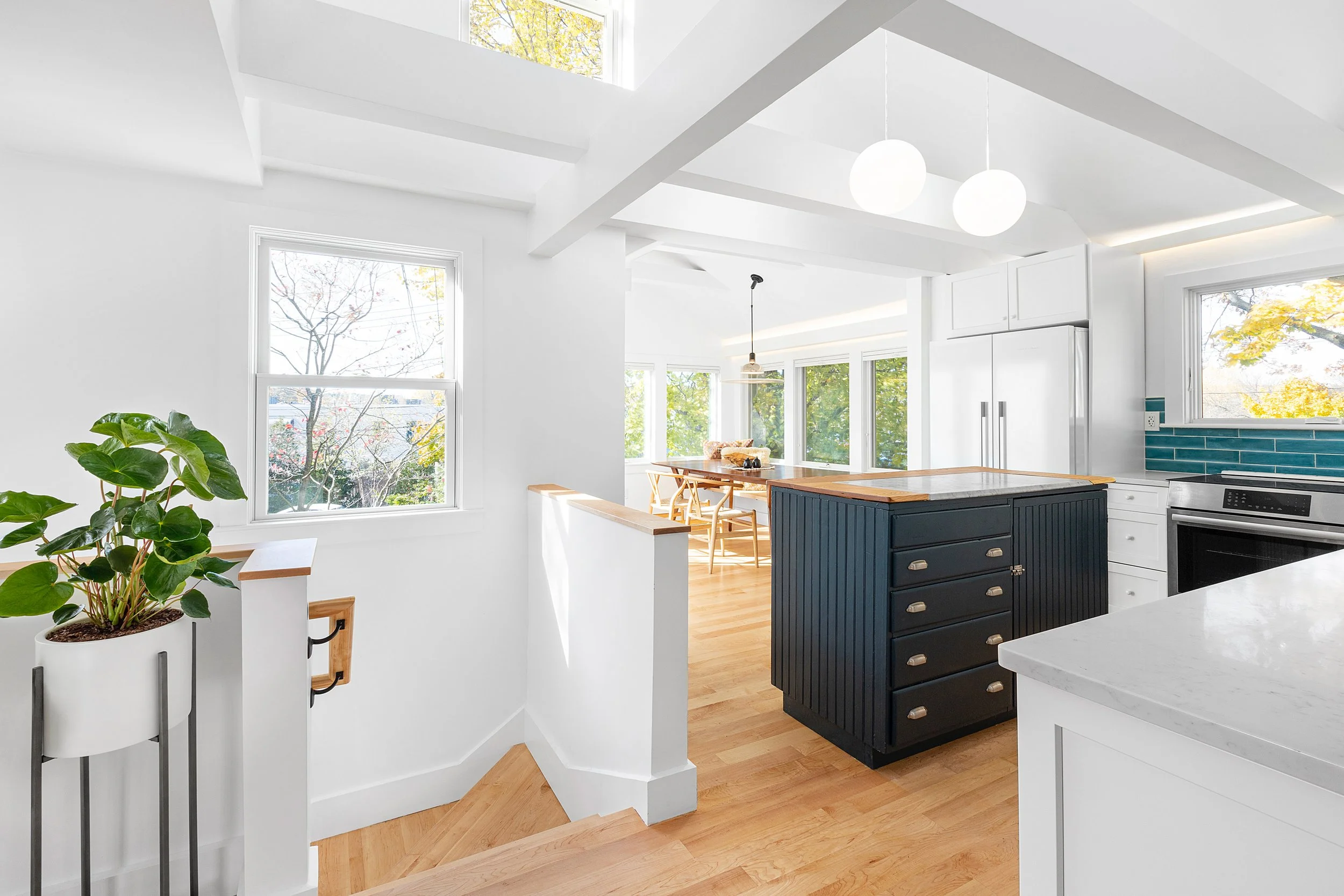 Bright, modern kitchen with white walls, large windows, a black kitchen island with drawers, and a view of a dining area with a table and chairs at the back.