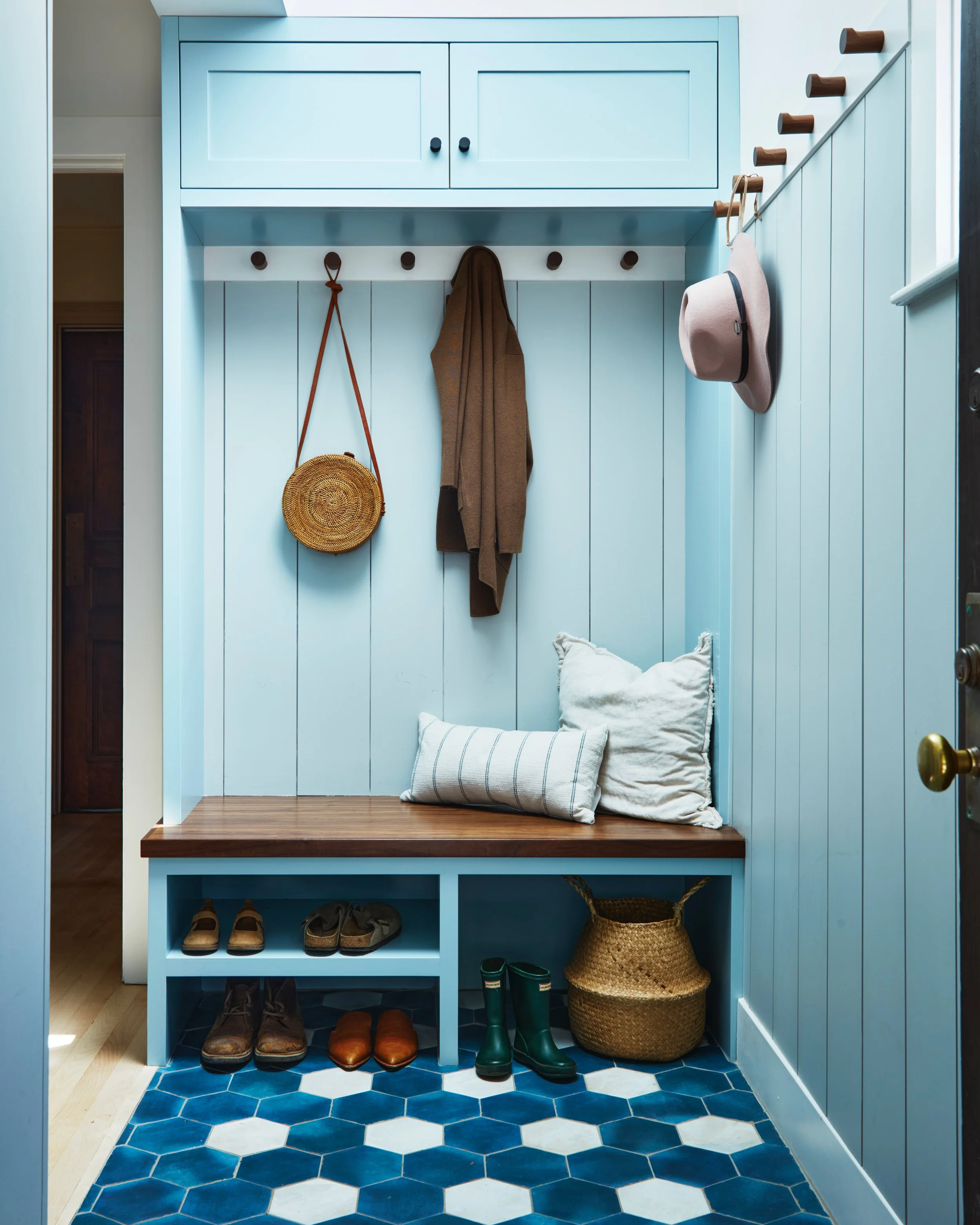 Light blue mudroom with coat hooks, a bench, and storage for shoes, with a blue hexagonal tiled floor.