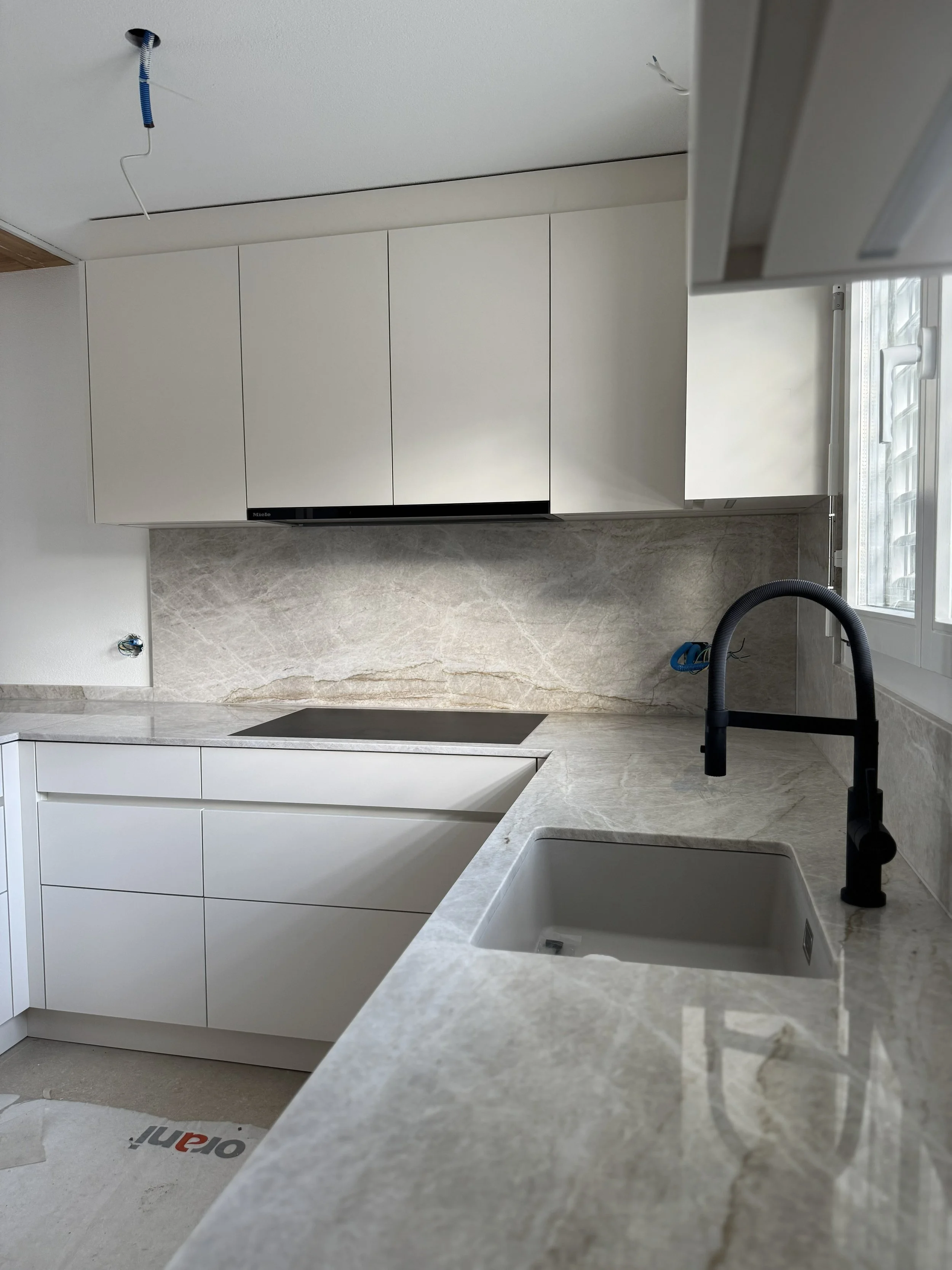 Modern weiße Küche mit schwarzem Wasserhahn und Eingang zu einem Fenster, die Küche ist noch im Bau.