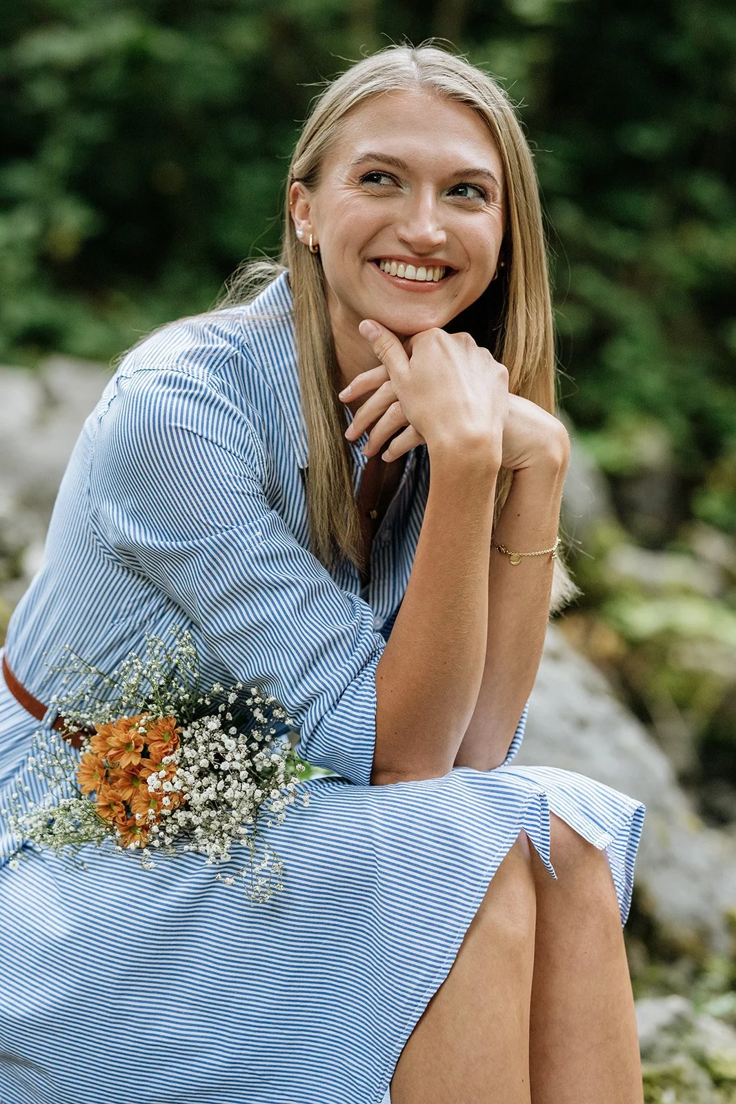 Outdoor Portrait am Rettenbach in Bad Ischl – junge Frau mit Blumen in der Hand grinst locker an der Kamera vorbei.