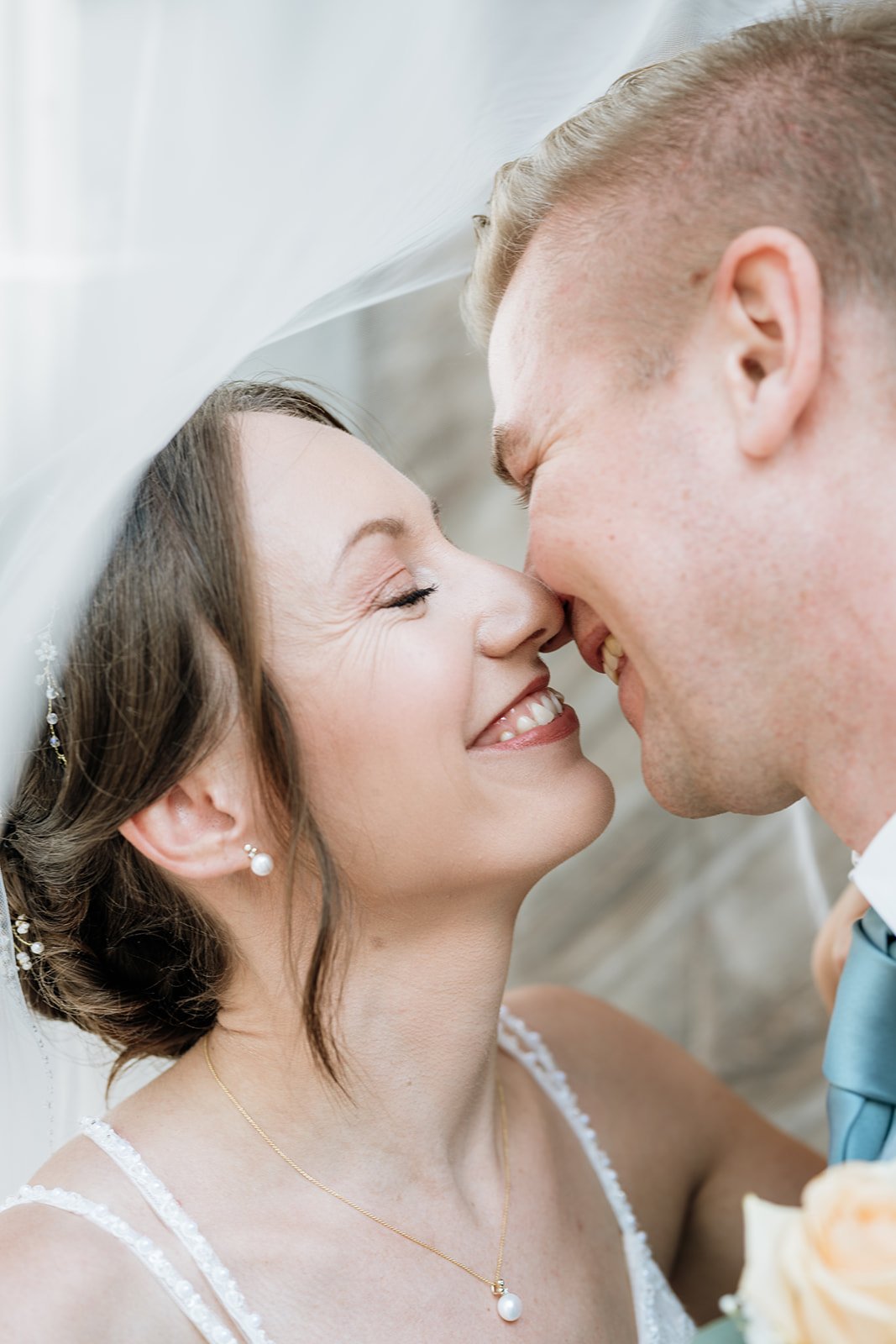 Braut und Bräutigam lächeln sich bei ihrer Hochzeit an, mit der Stirn aneinander.