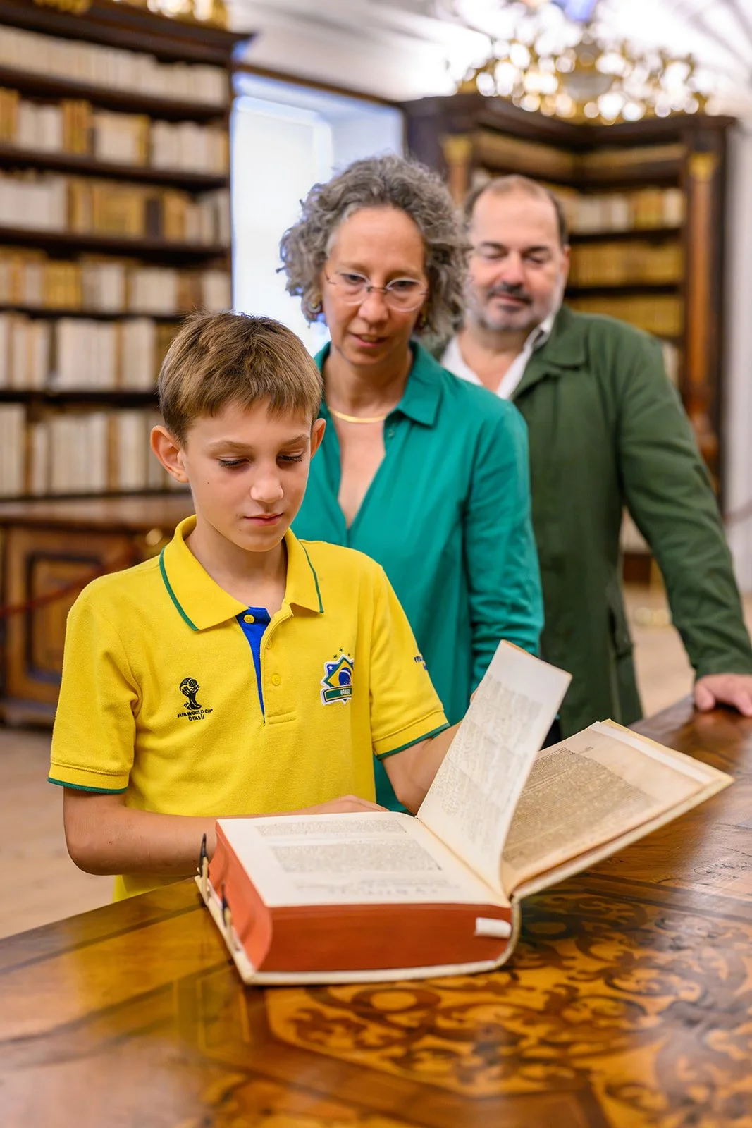 Junger Besucher betrachtet mit seinen Eltern ein aufgeschlagenes Buch in der Stiftsbibliothek Kremsmünster